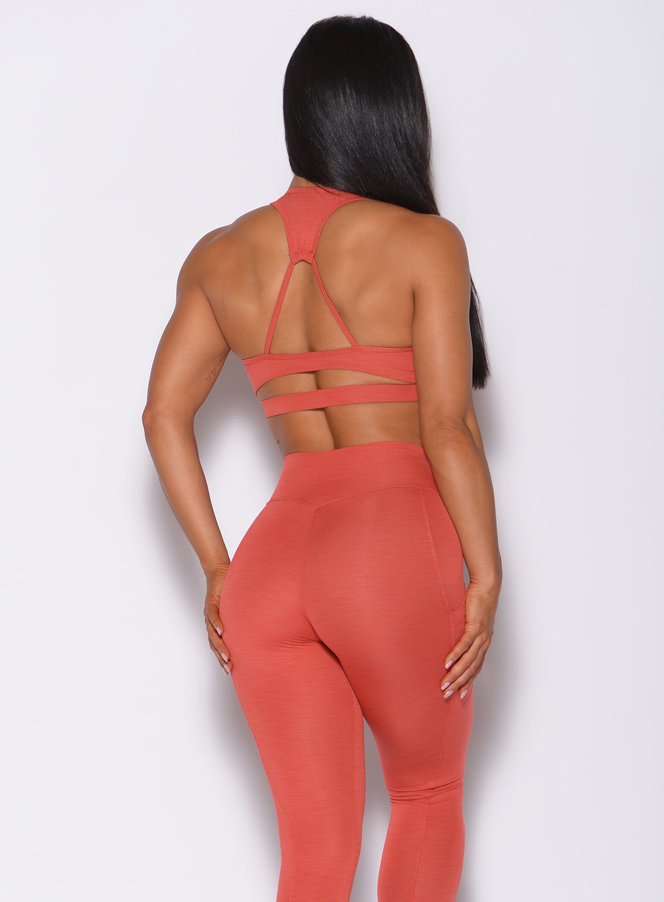 Back profile view of a model wearing our power rib sports bra in burnt orange color and a matching high rise leggings