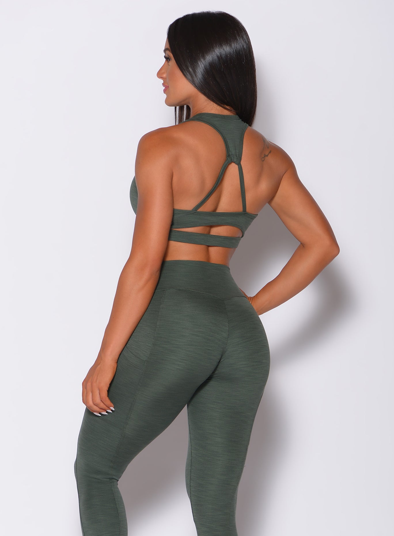 Back profile view of a model in our power rib sports bra in forest green color and a matching leggings