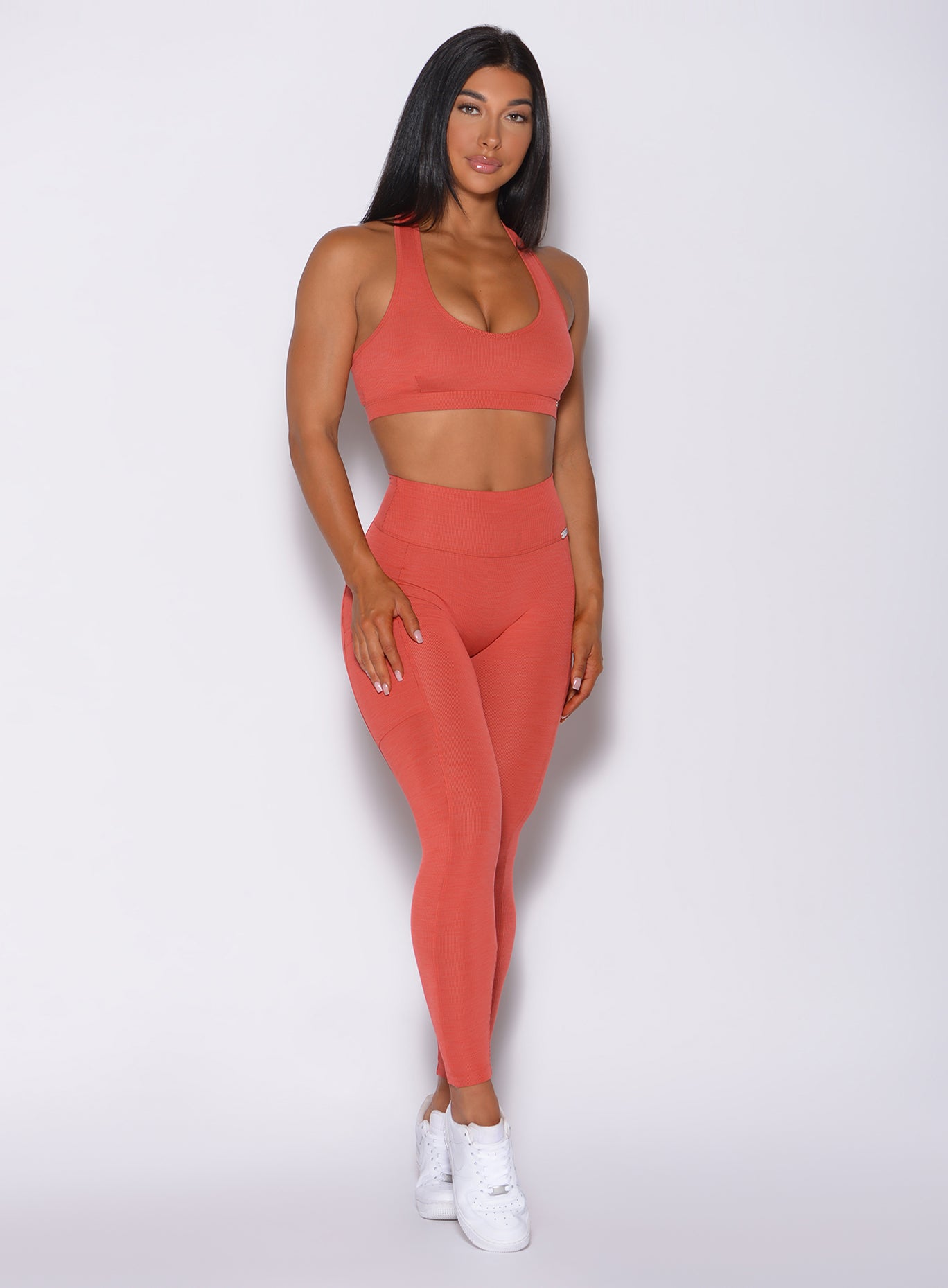 Front profile view of a model facing forward wearing our pocket rib leggings in burnt orange color and a matching bra