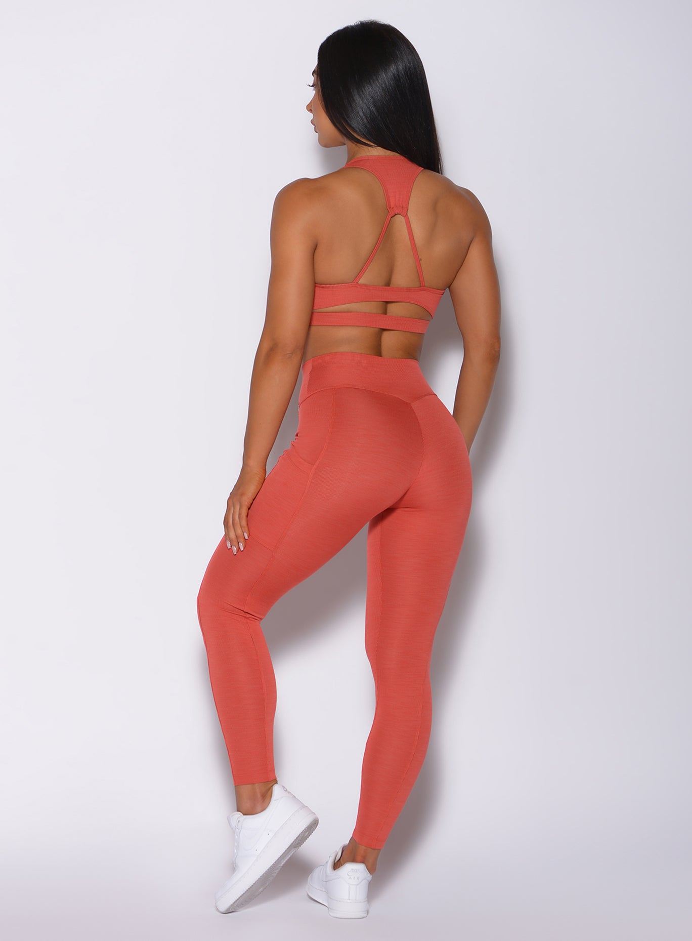 Back profile view of a model in our pocket rib leggings in burnt orange color and a matching sports  bra