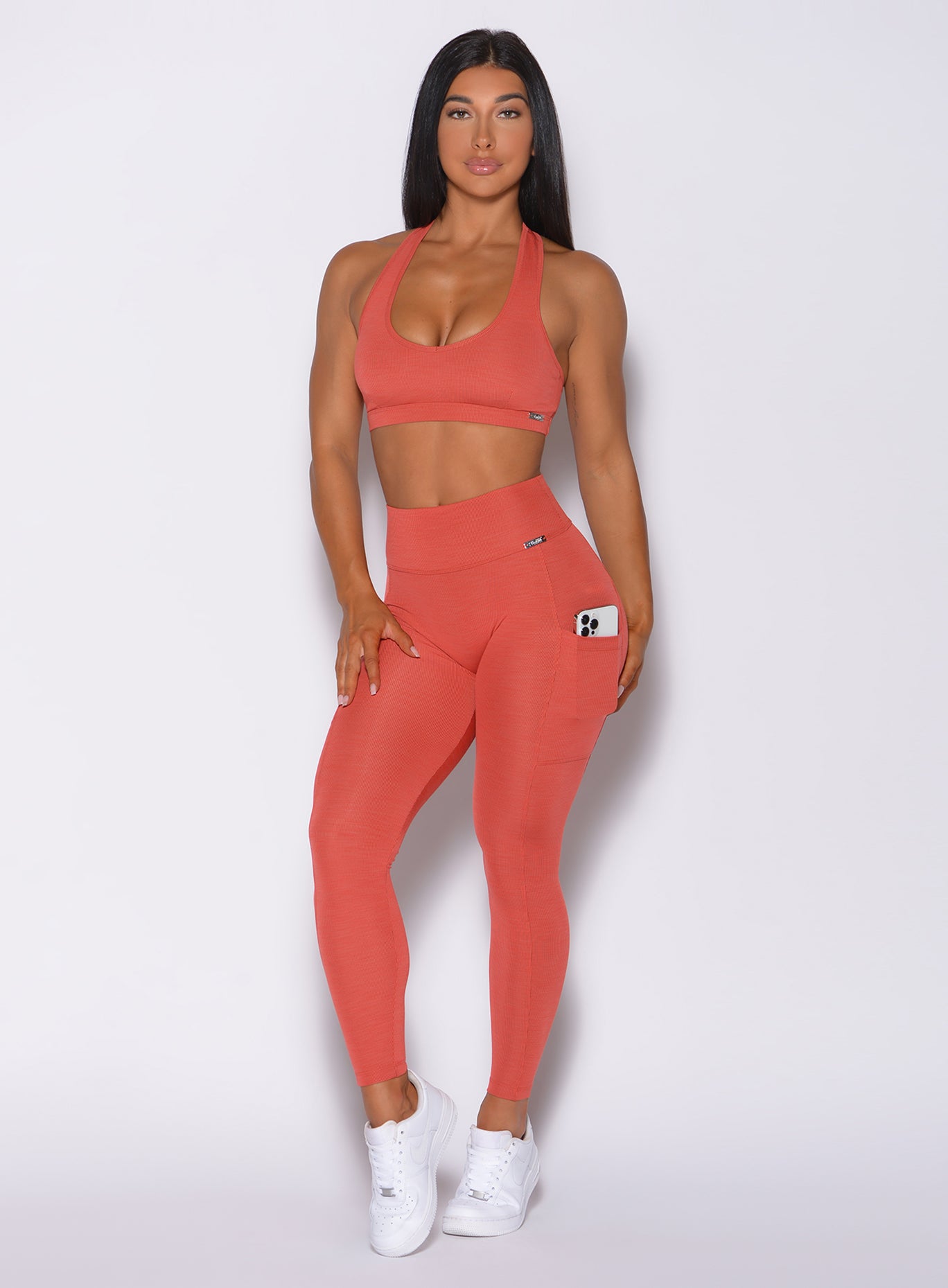 Model facing forward wearing our pocket rib leggings in burnt orange color and a matching bra