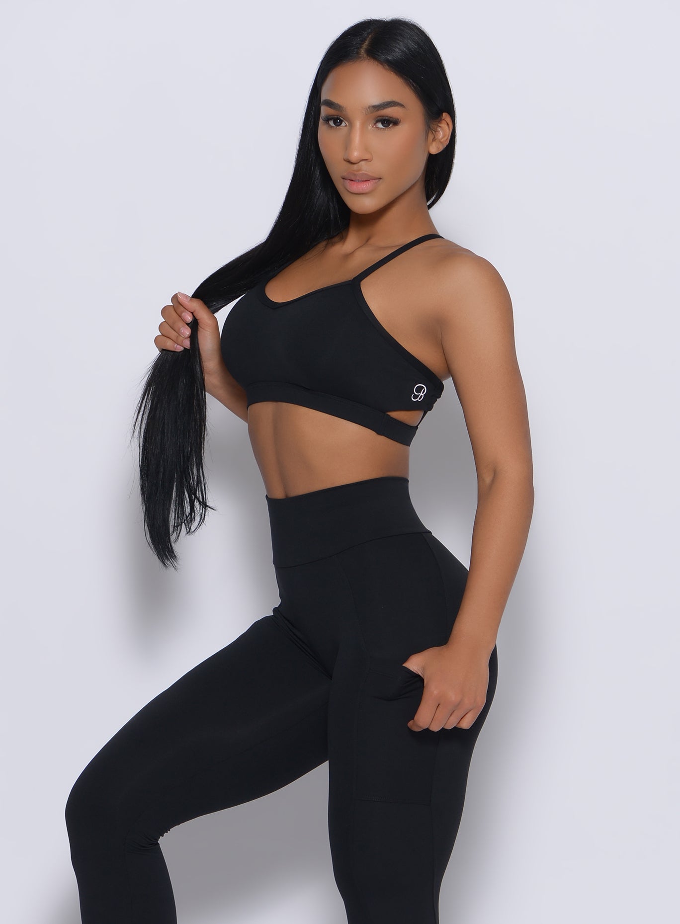 Left side profile view of a model holding her hair wearing our black pumped sports bra and a matching leggings