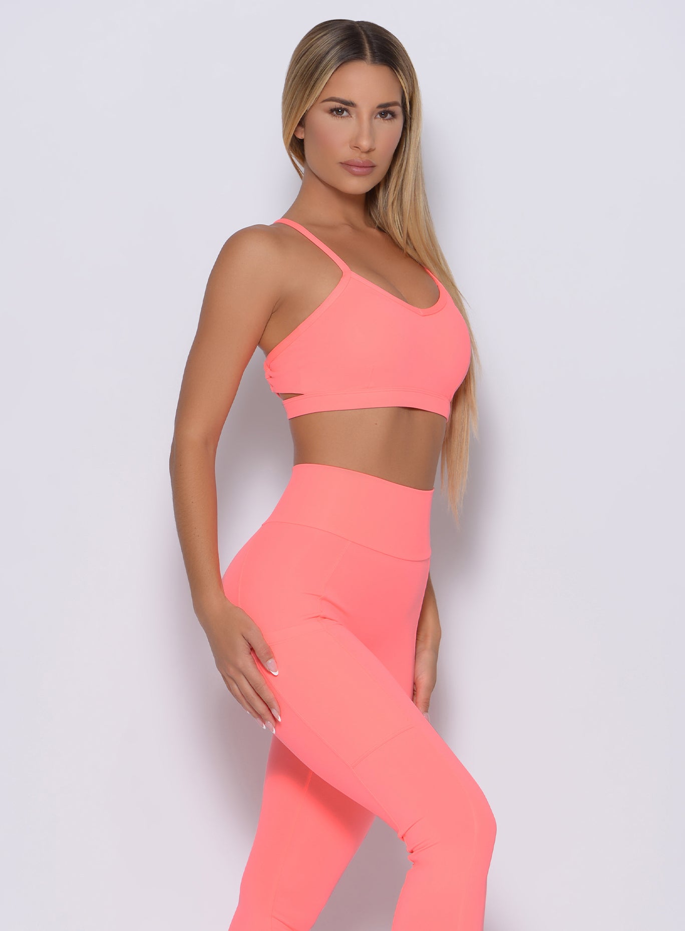 Right side profile view of a model in our pumped sports bra in wild peach color and a matching leggings