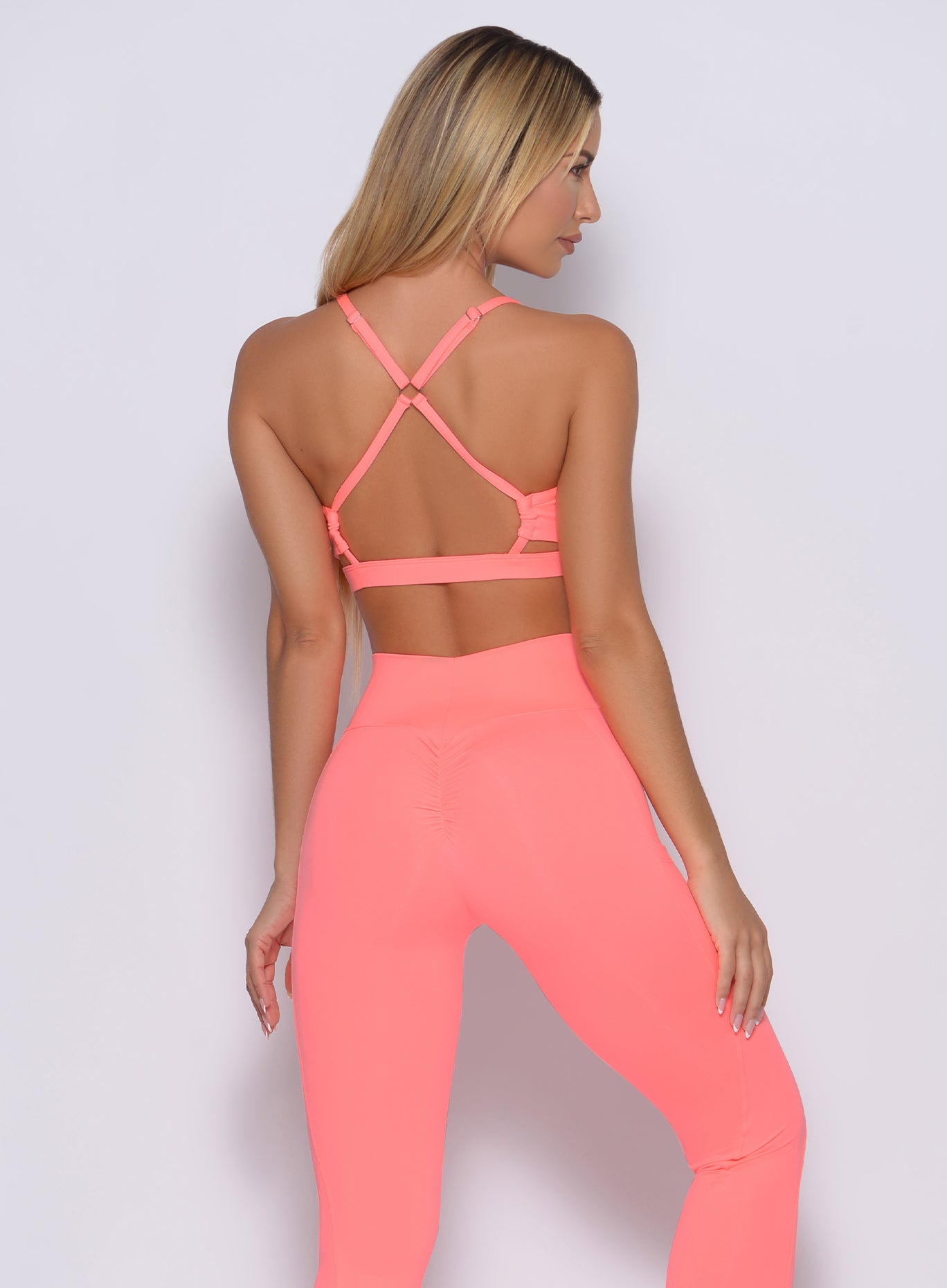 Back profile view of a model in our pumped sports bra in wild peach color and a matching leggings