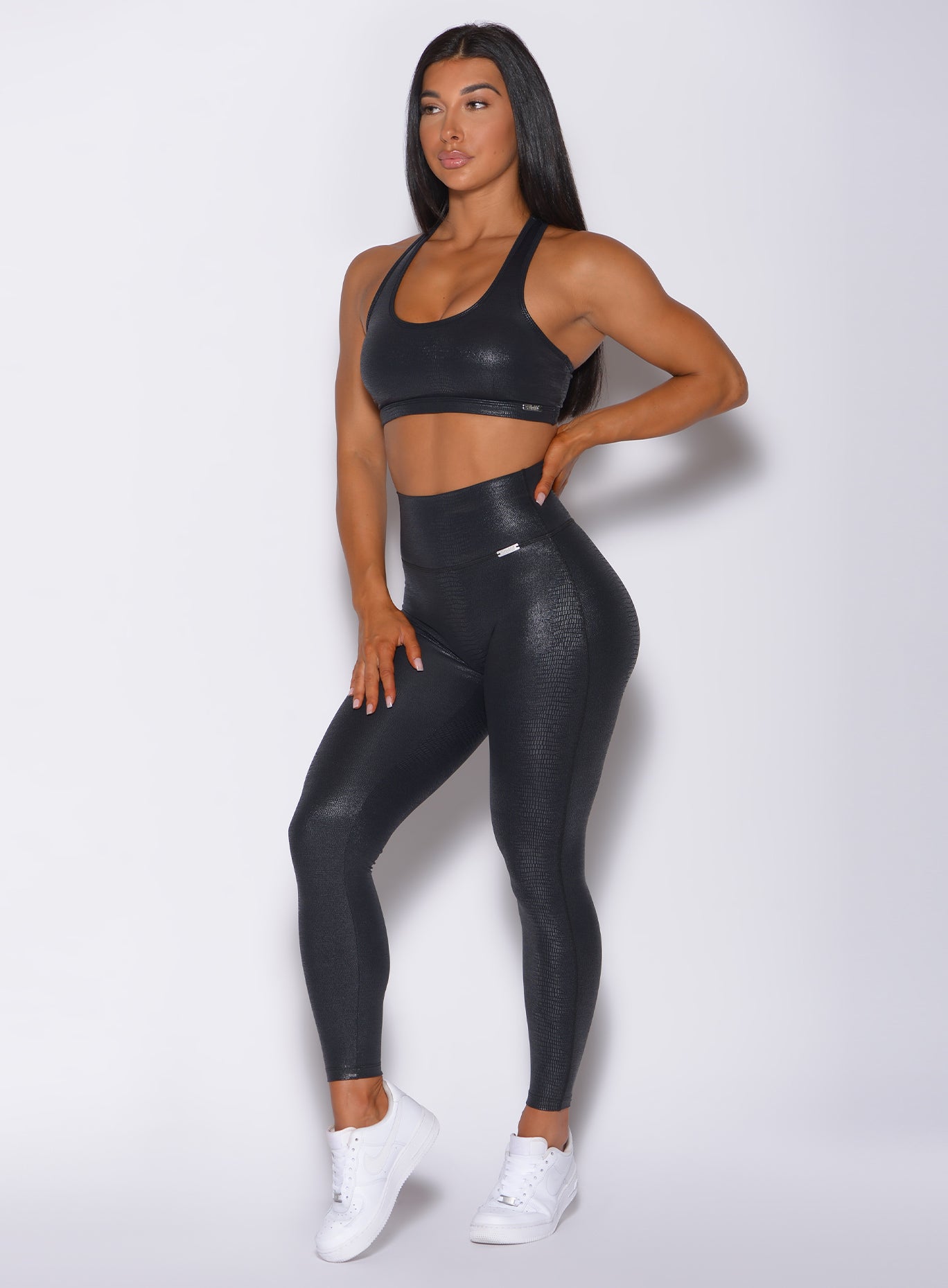 Left side profile view of a model  angled left wearing our shine leggings in black python color and a matching sports bra