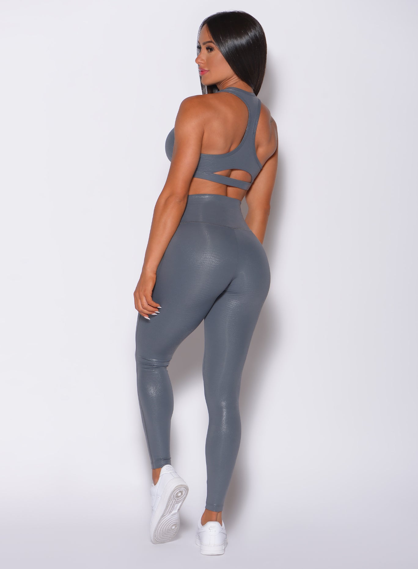 Back profile view of a model angled right wearing  our shine leggings in gray python color and a matching bra