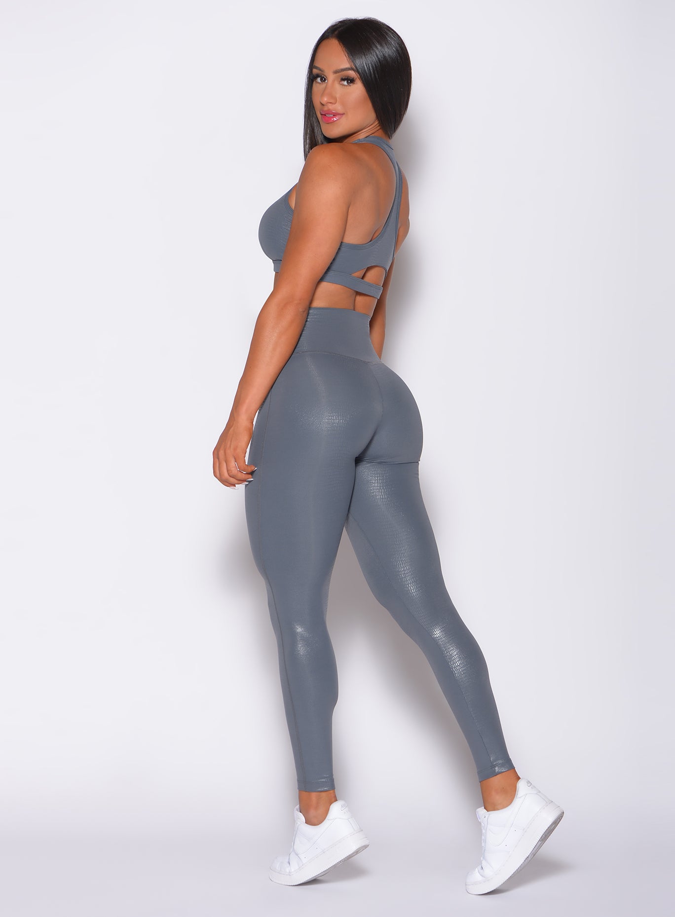 Left side profile view of a model facing to her left wearing our shine leggings in gray python color and a matching bra