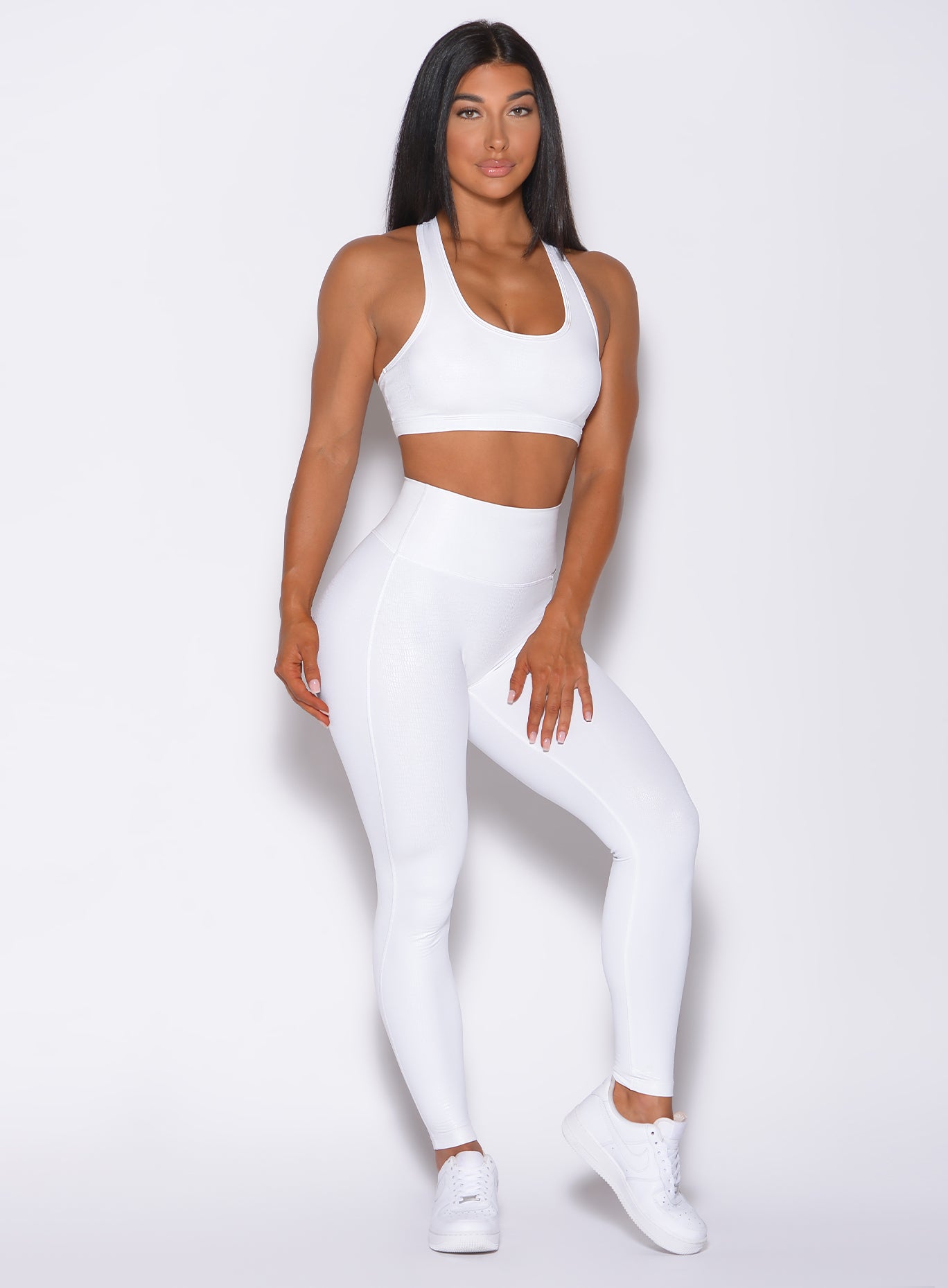 Front profile view of a model facing forward wearing our shine leggings in white python color and a matching bra