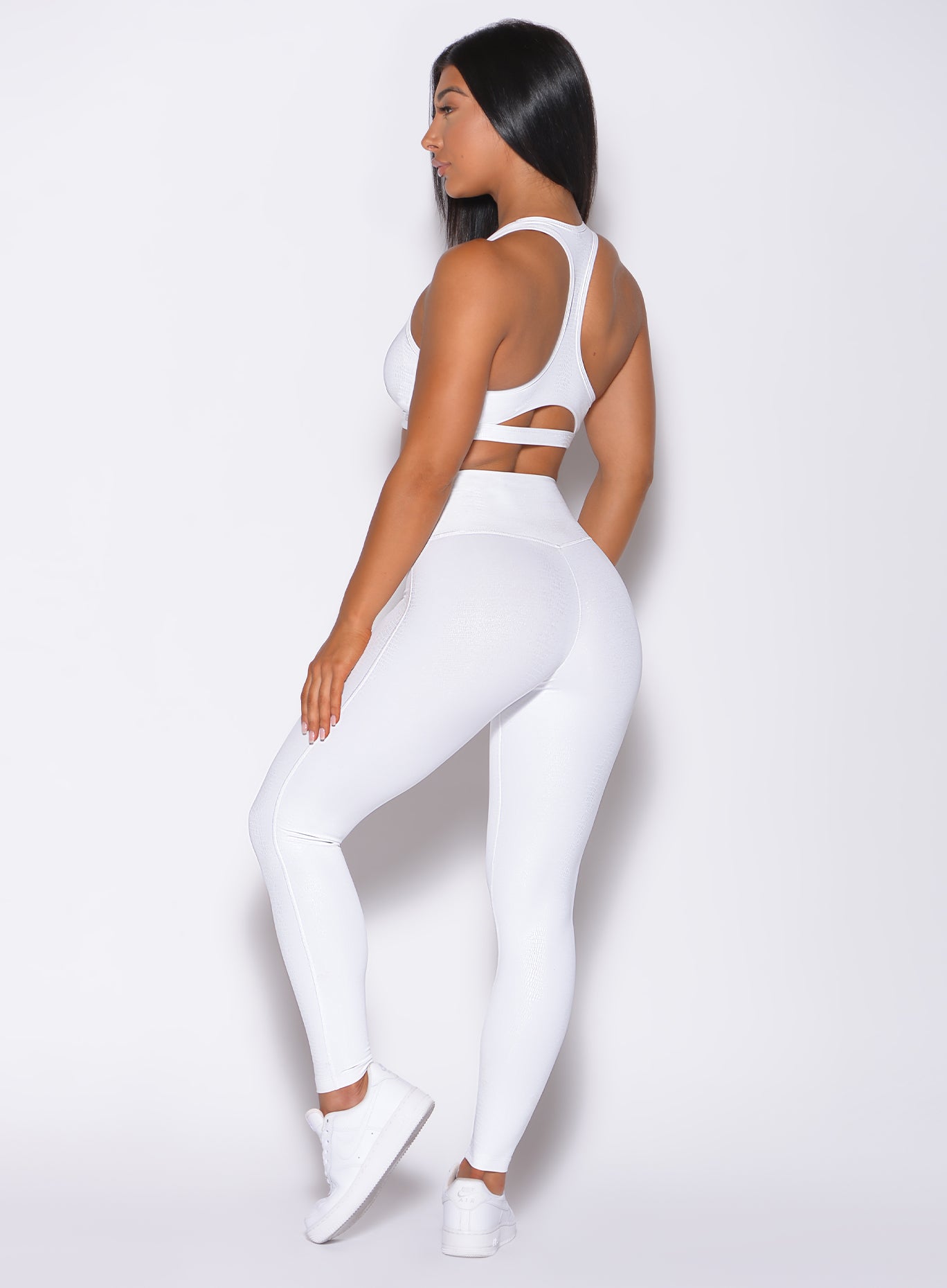 Left side profile view of a model in our shine leggings in white python color and a matching bra