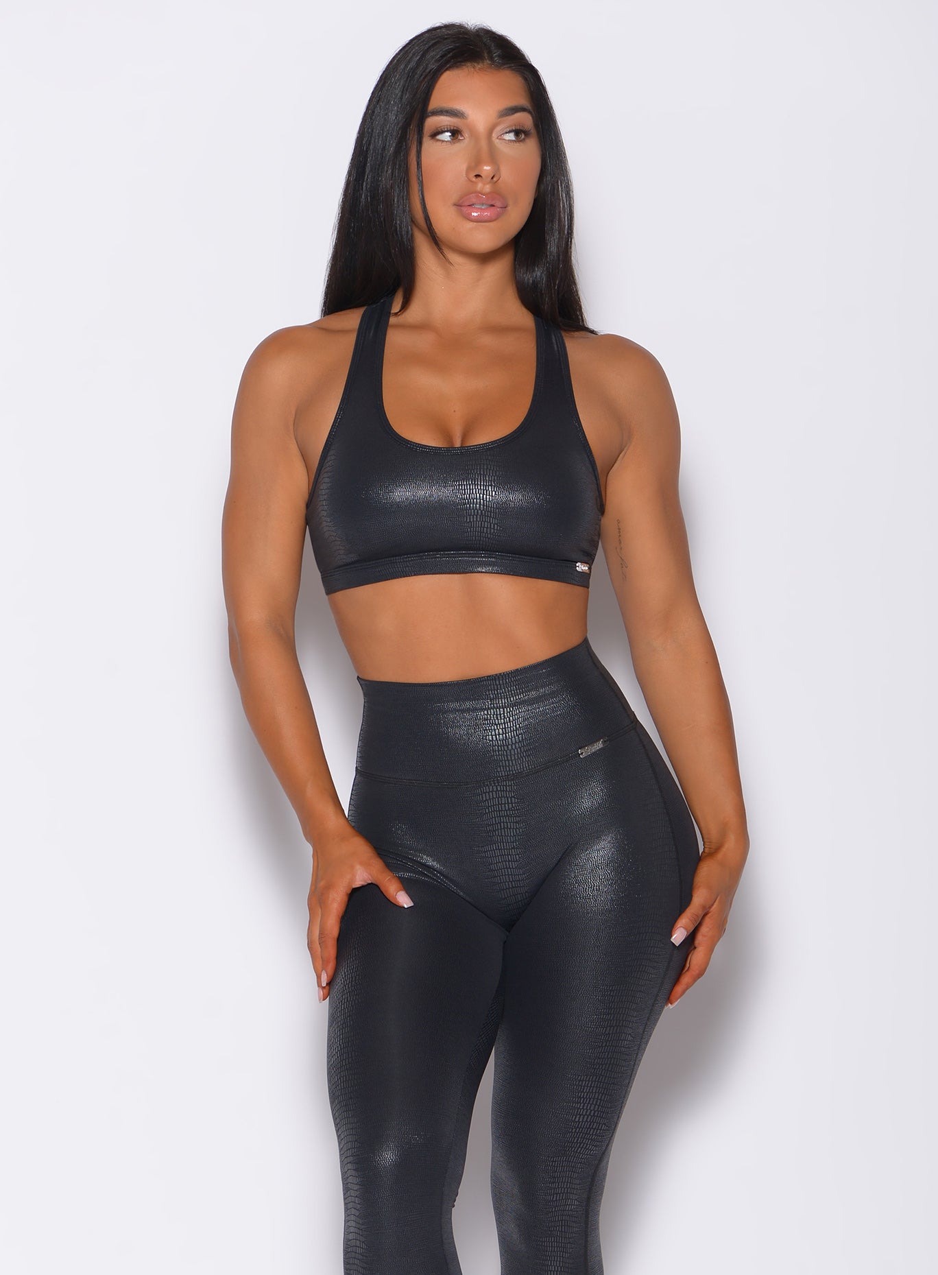 Front profile view of a model facing to her left wearing our shine sports bra in black python color and a matching leggings