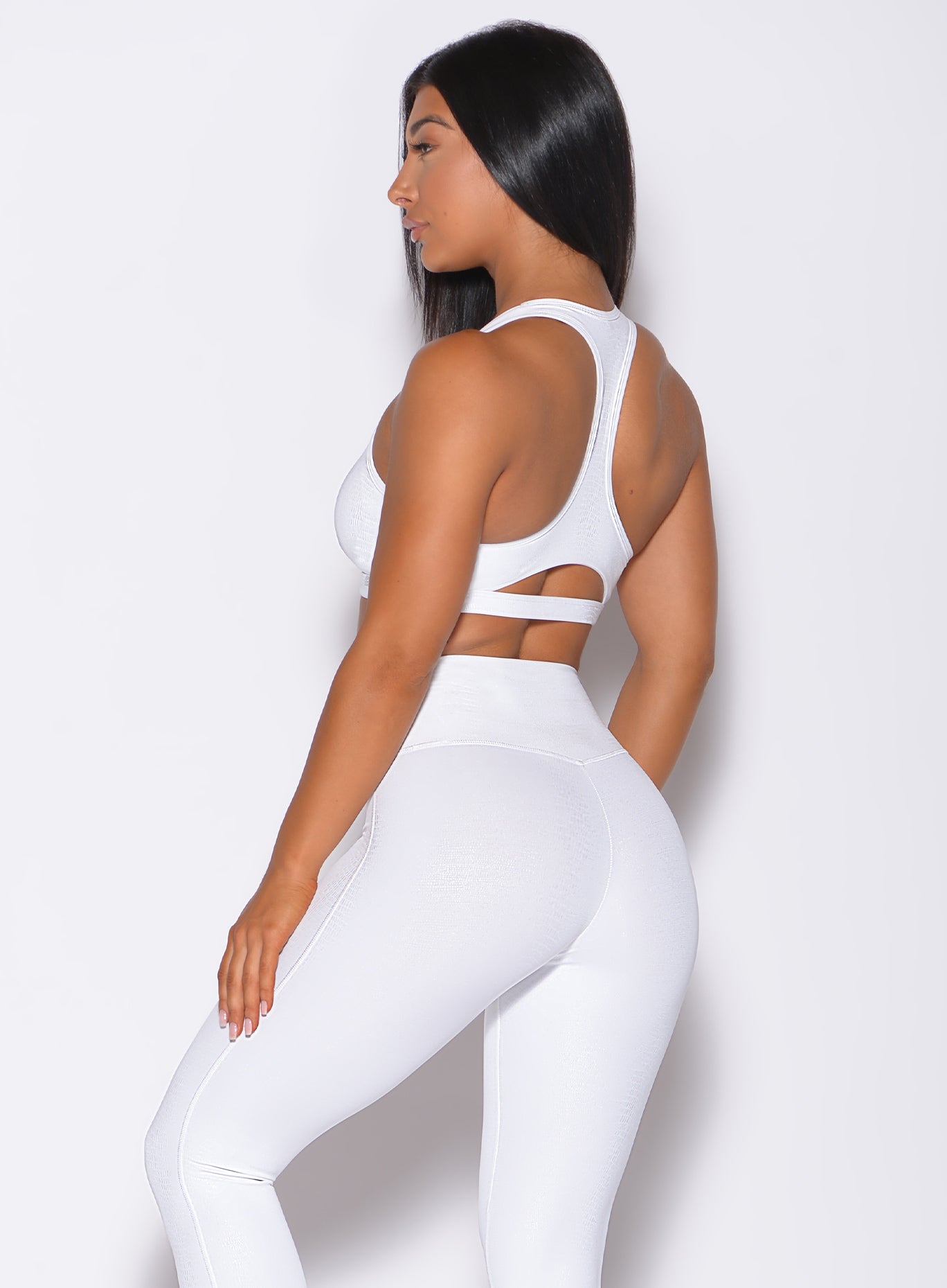 Left side profile view of a model wearing our shine sports bra in white python color and a matching leggings