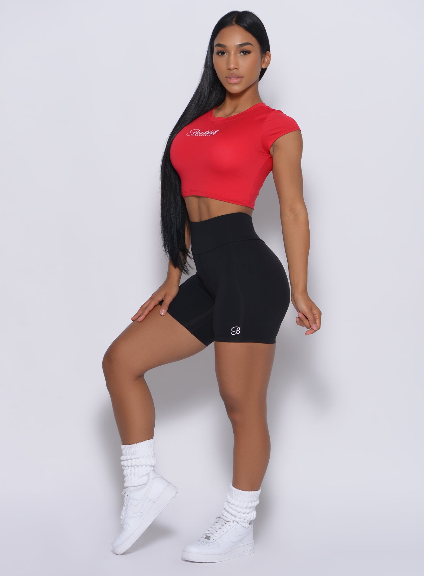 Left side profile view of a model  angled left wearing our black refined shorts and a red top 