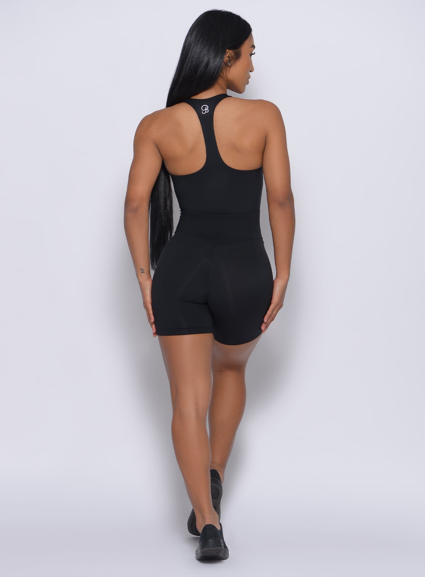 Back profile view of the model wearing our black refined shorts and a matching bodysuit 