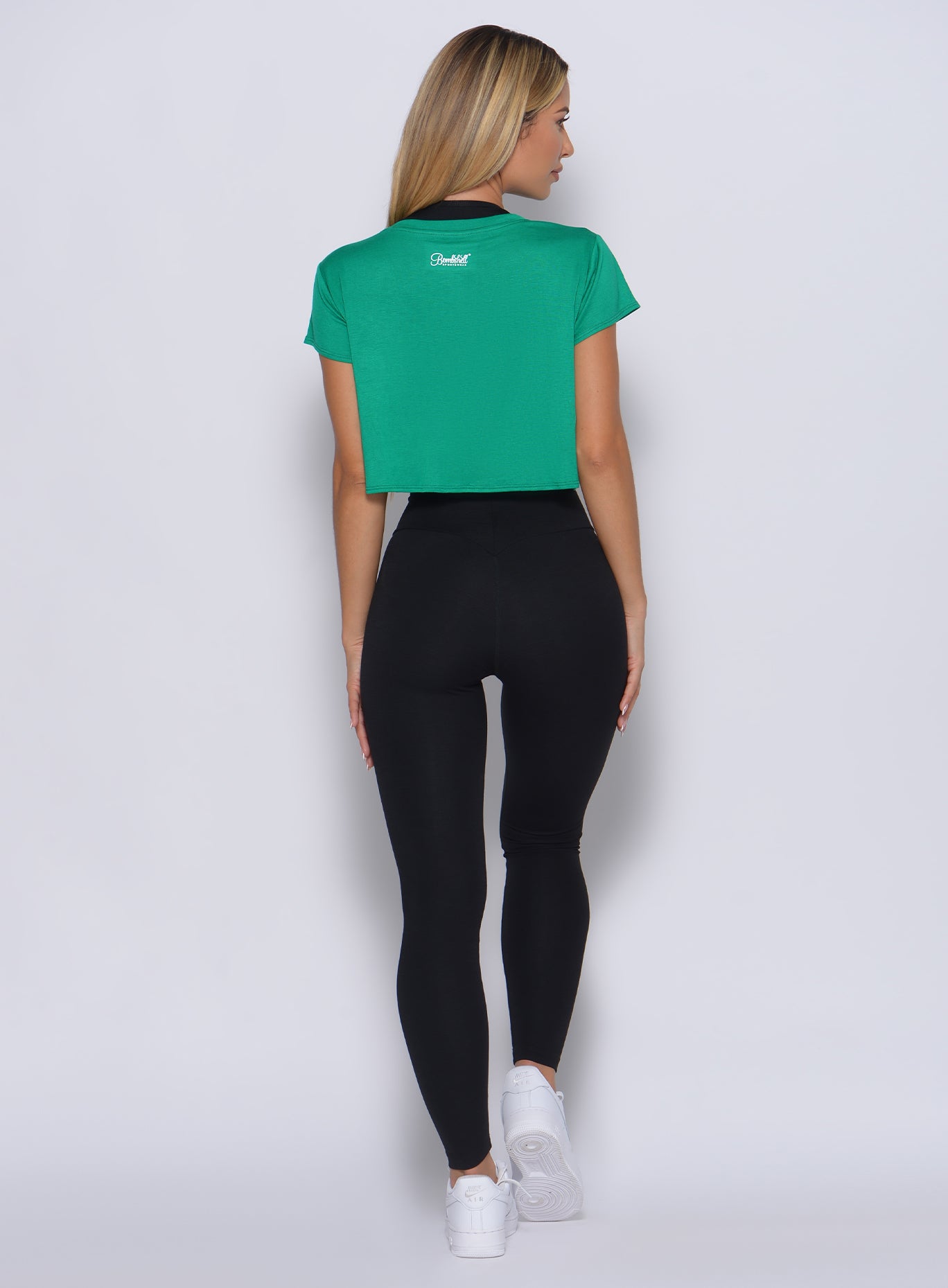 Back profile view of the model facing to her right wearing our freedom tee in apple green color and a black leggings