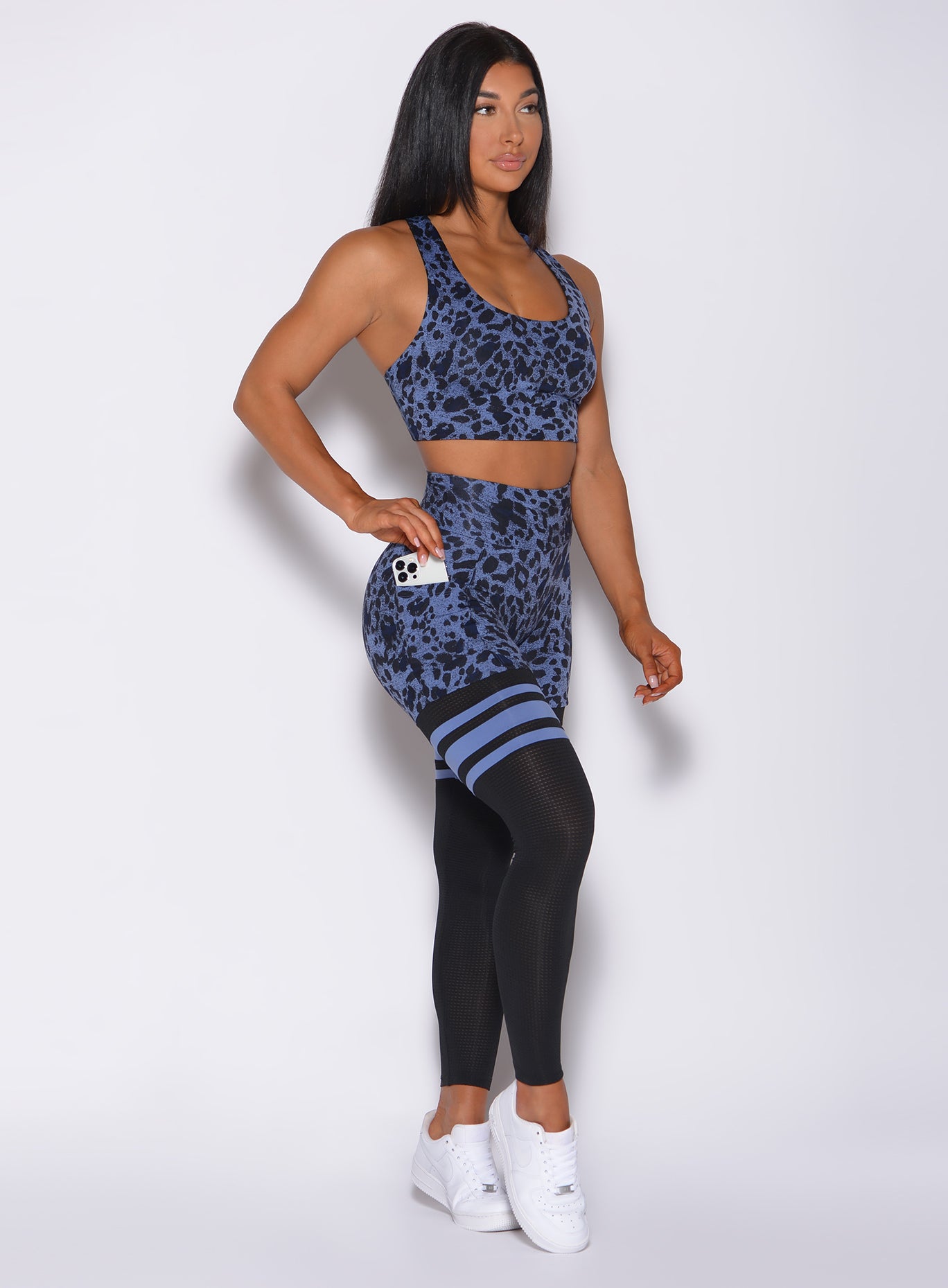 Right side profile view of a model facing forward wearing our scrunch thigh high in blue leopard print and a matching sports bra