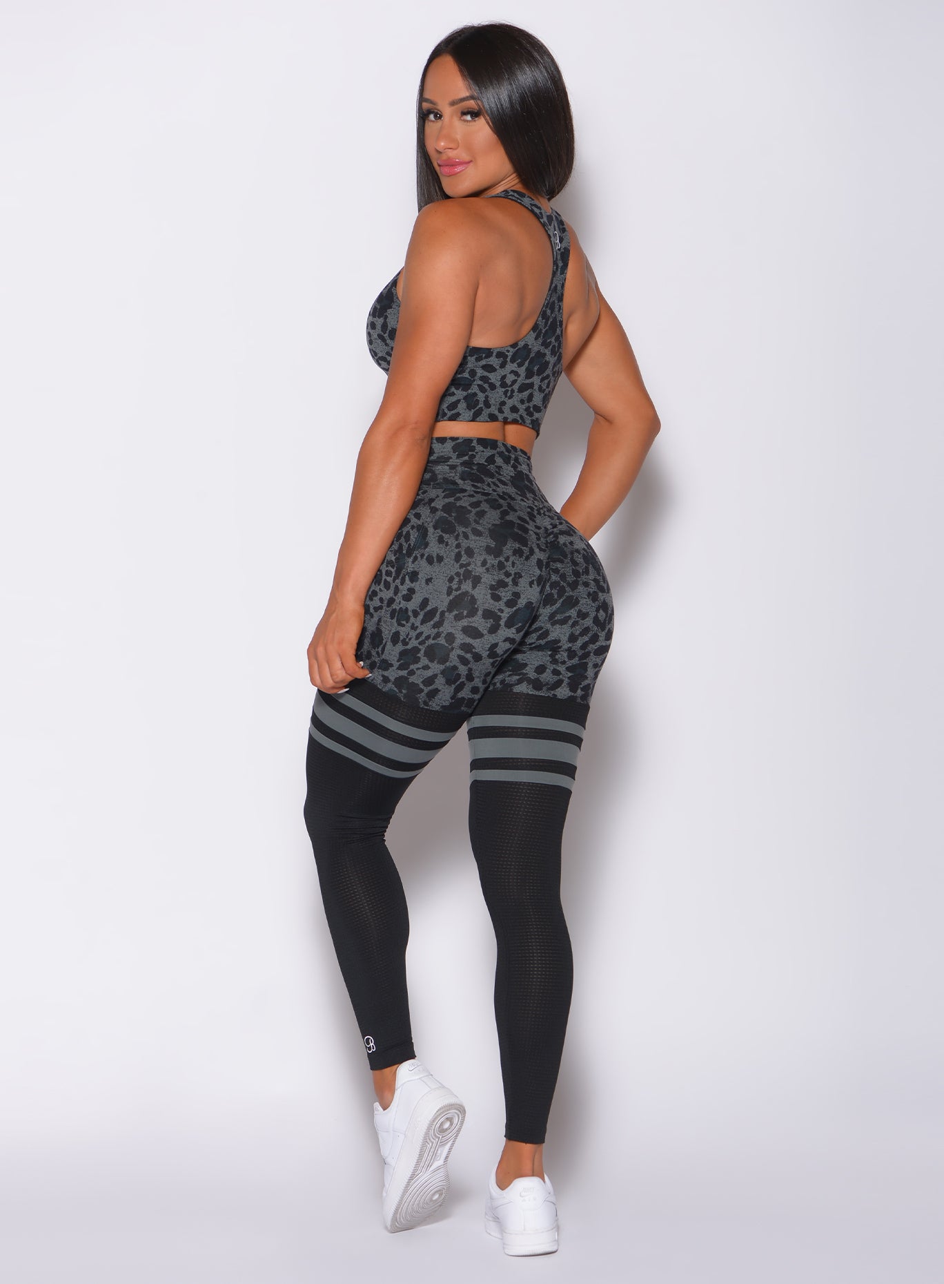 Left side profile view of a model in our scrunch thigh high in charcoal leopard print and a matching sports bra 