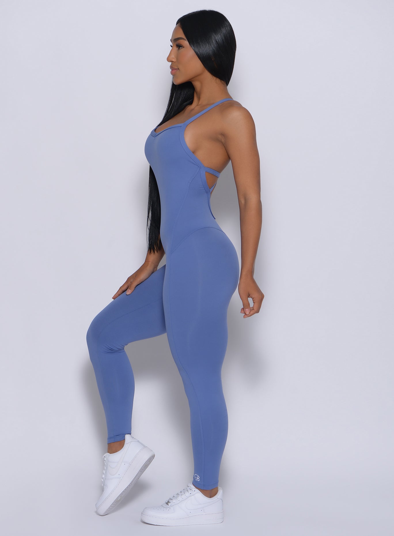 Left side profile view of the model with her right hand on thigh wearing our sculpted bodysuit in denim blue color 