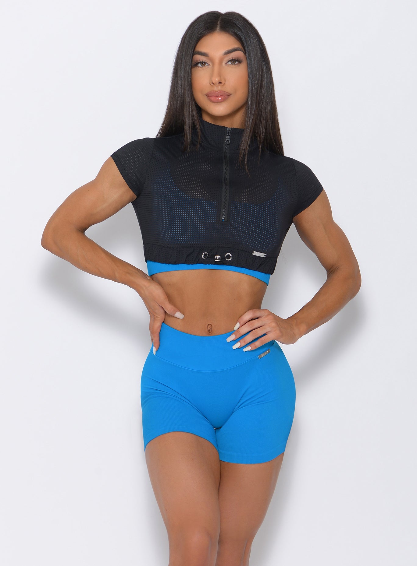 Front view of the model with her hands on wait wearing our black glow up top and a blue shorts 