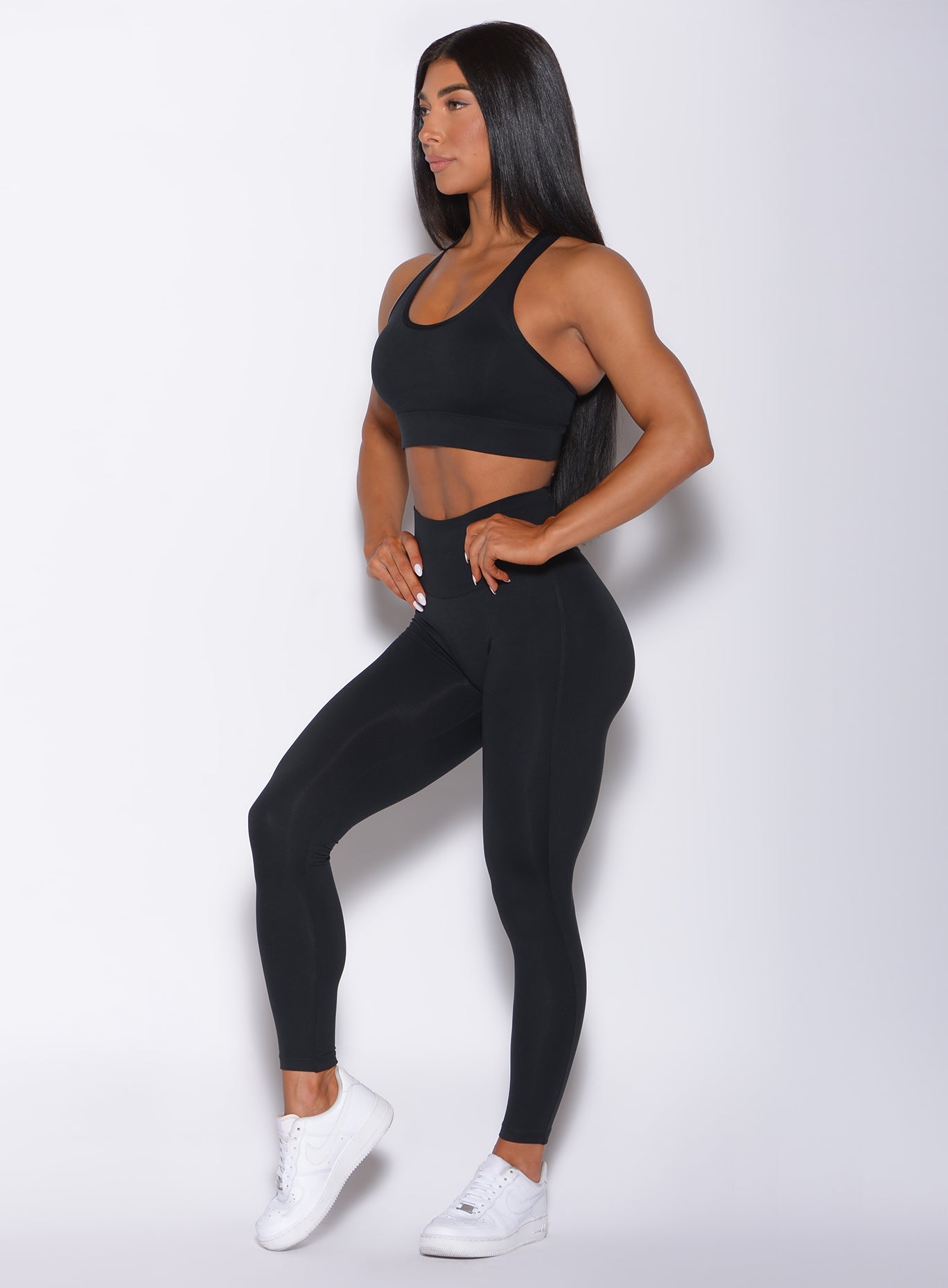 Left side profile picture of a model facing forward wearing our black sexy back leggings  along with a matching bra 
