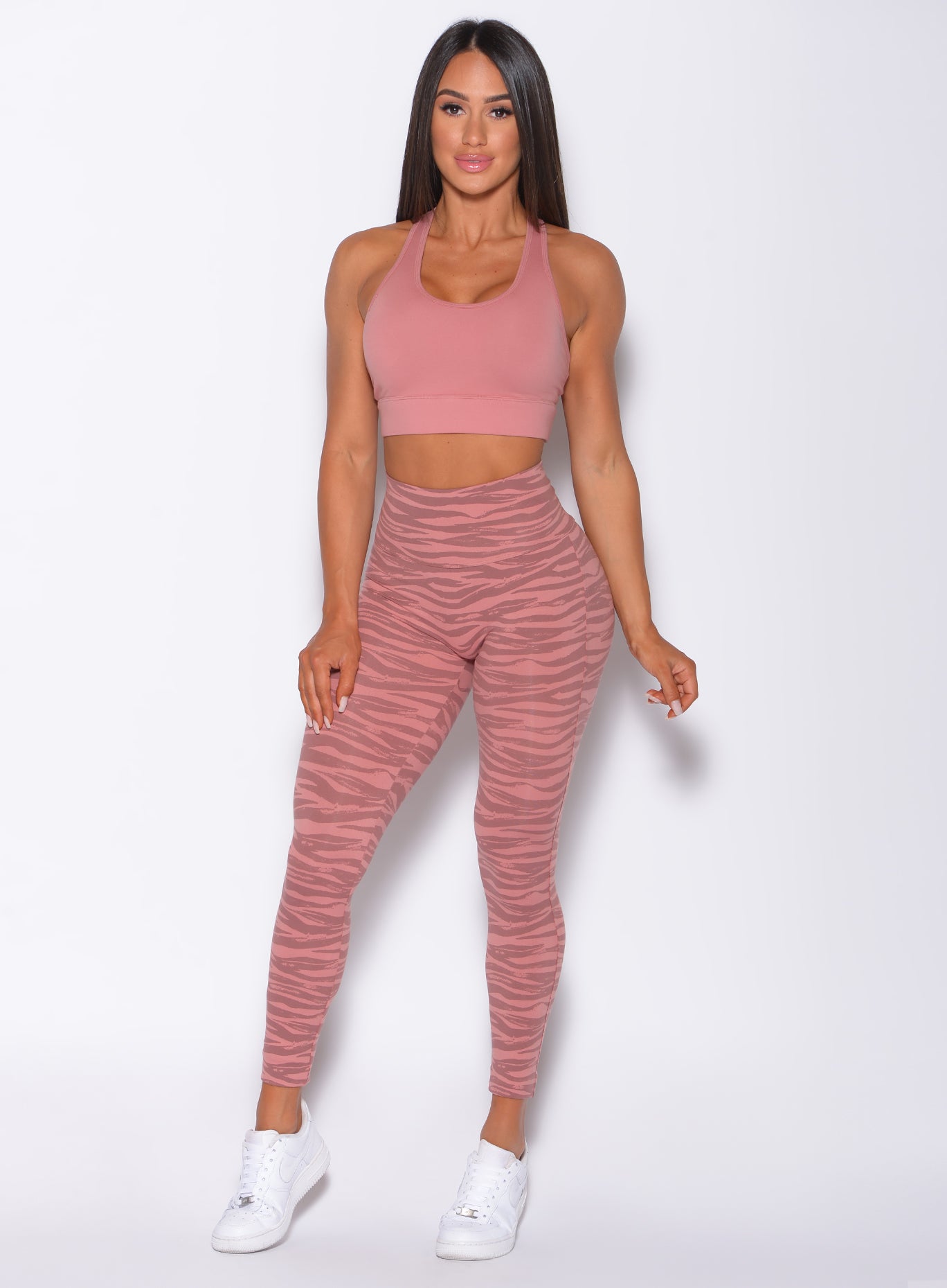 Model facing forward wearing our rival sports bra in solid blush color and a matching tiger print leggings