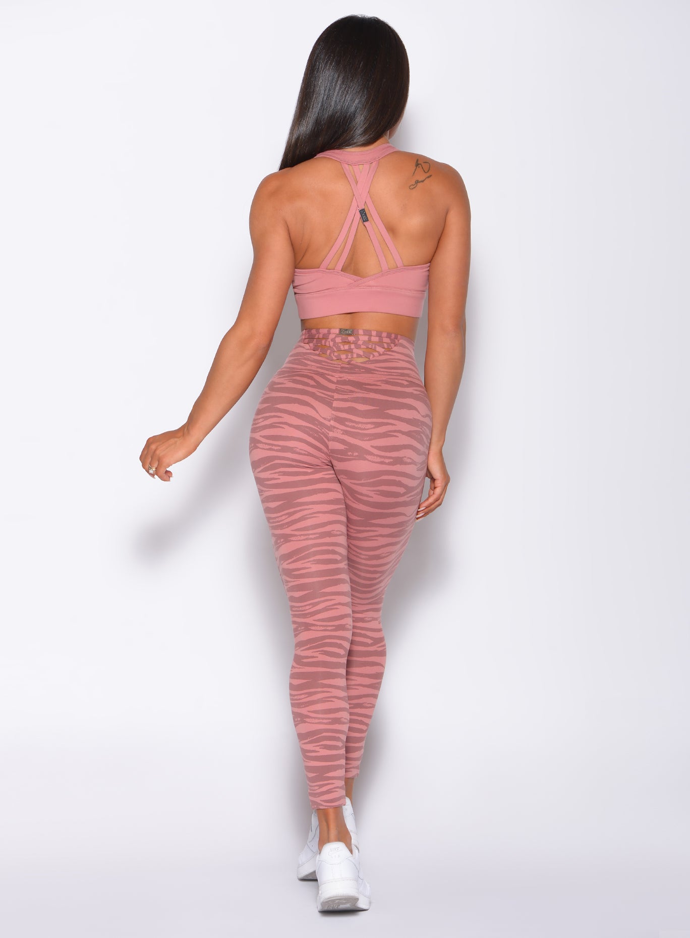 Back profile view of a model in our rival sports bra in solid blush color and a matching tiger print sexy back leggings