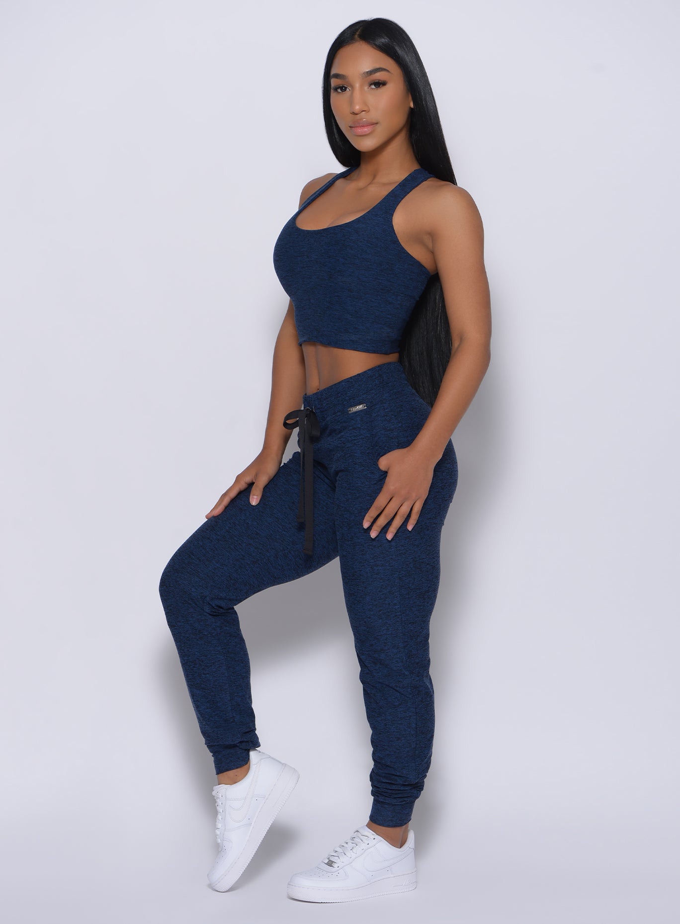 Left side profile view of a model angled left wearing our signature joggers in sapphire blue color and a matching bra