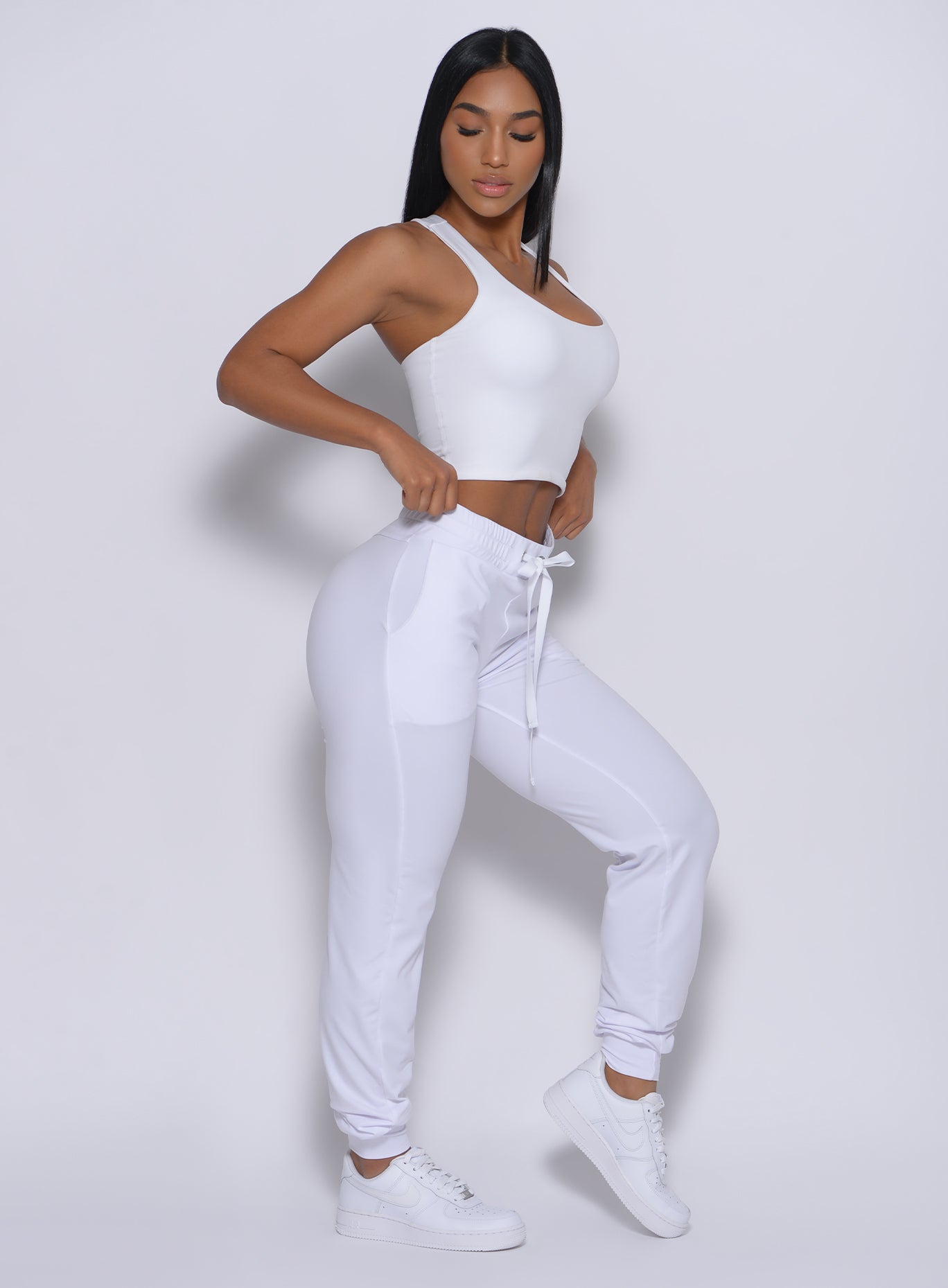 Right side  profile view of a model facing to her right wearing our white elevated tank bra and a matching joggers