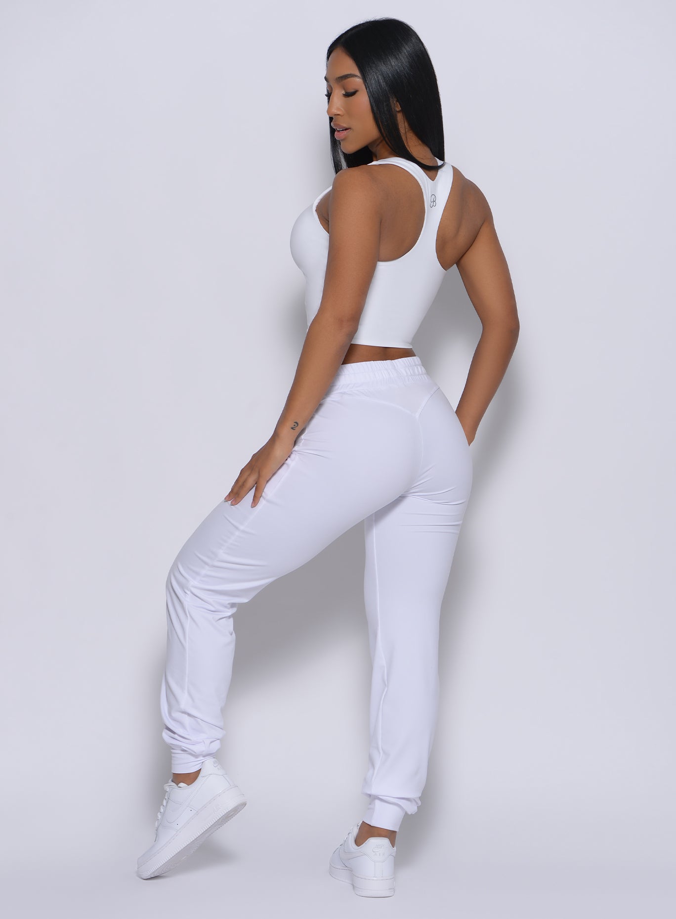 Left side profile view of a model angled right wearing our white signature joggers and a matching bra