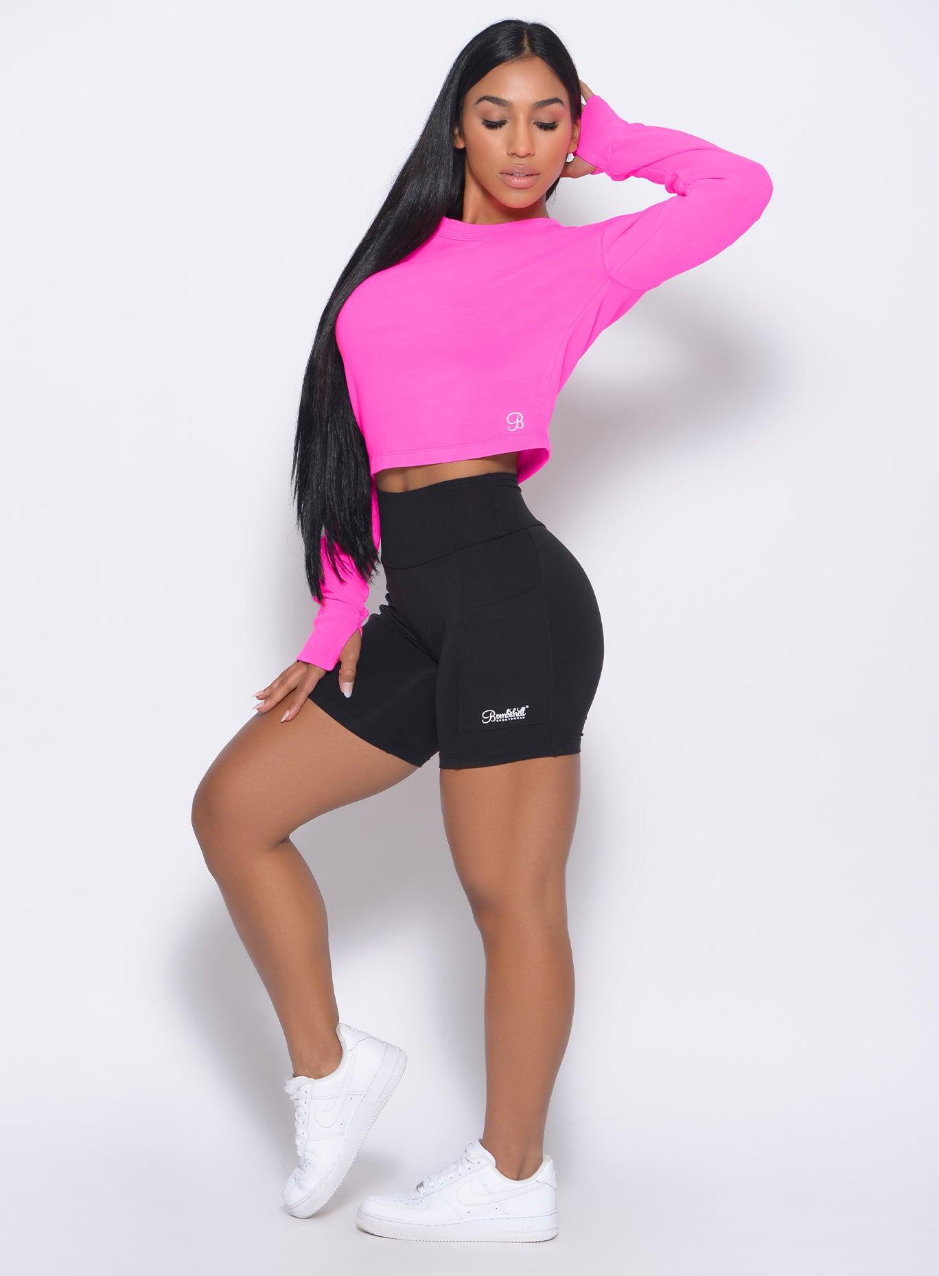 Left side view of the model in our black pocket biker shorts and a neon pink pullover