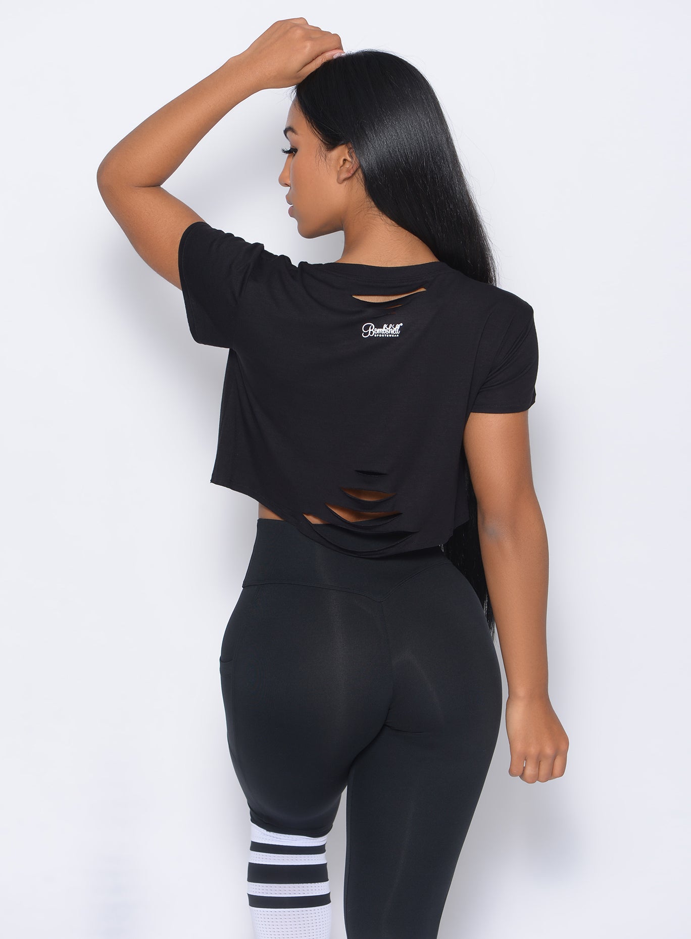 Back view of the model with her left hand over her head in our black shredded tee and a matching leggings
