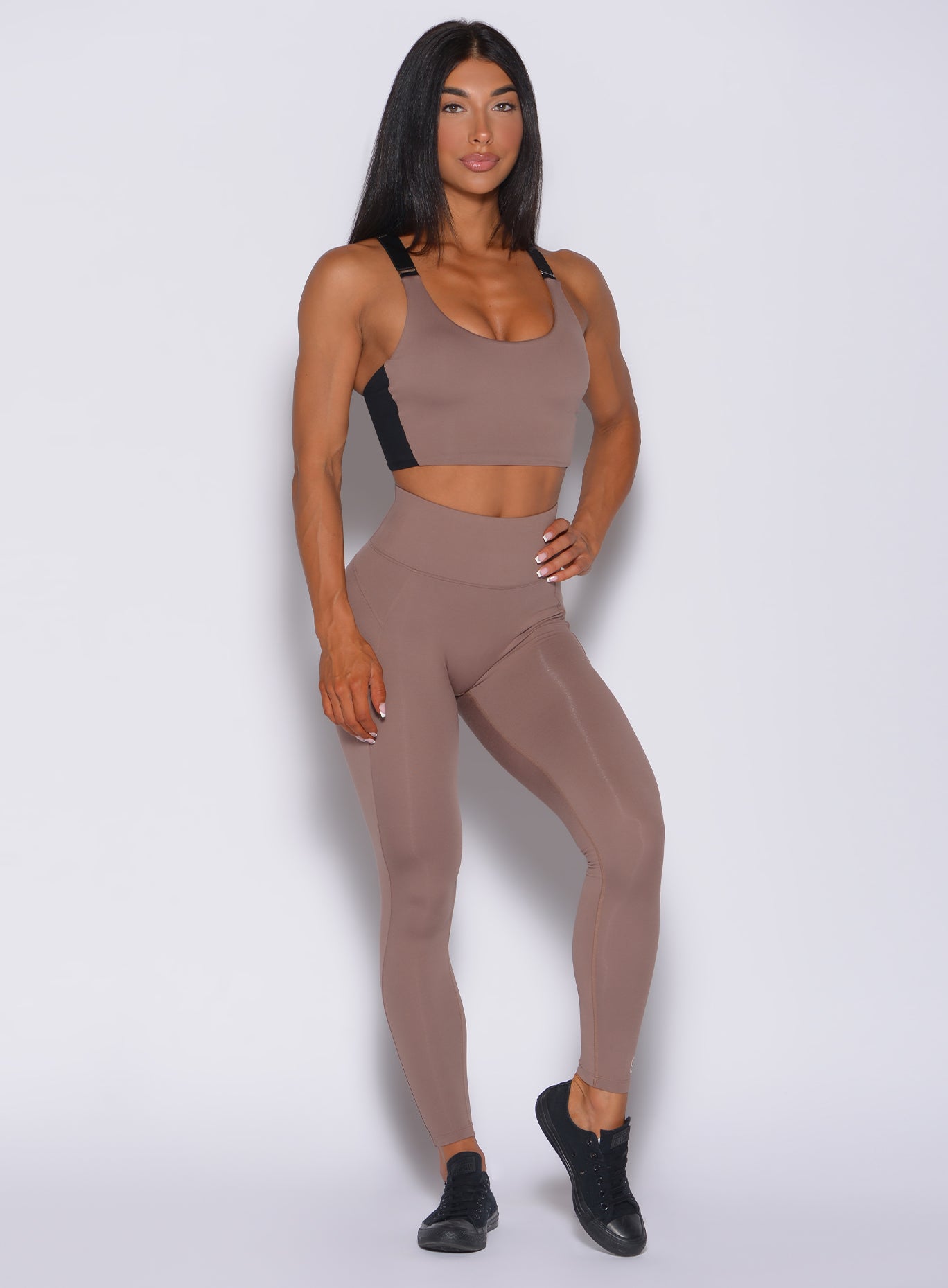 Front profile view of a model  with her left hand on waist wearing our snatched waist leggings in cocoa color and a matching bra 