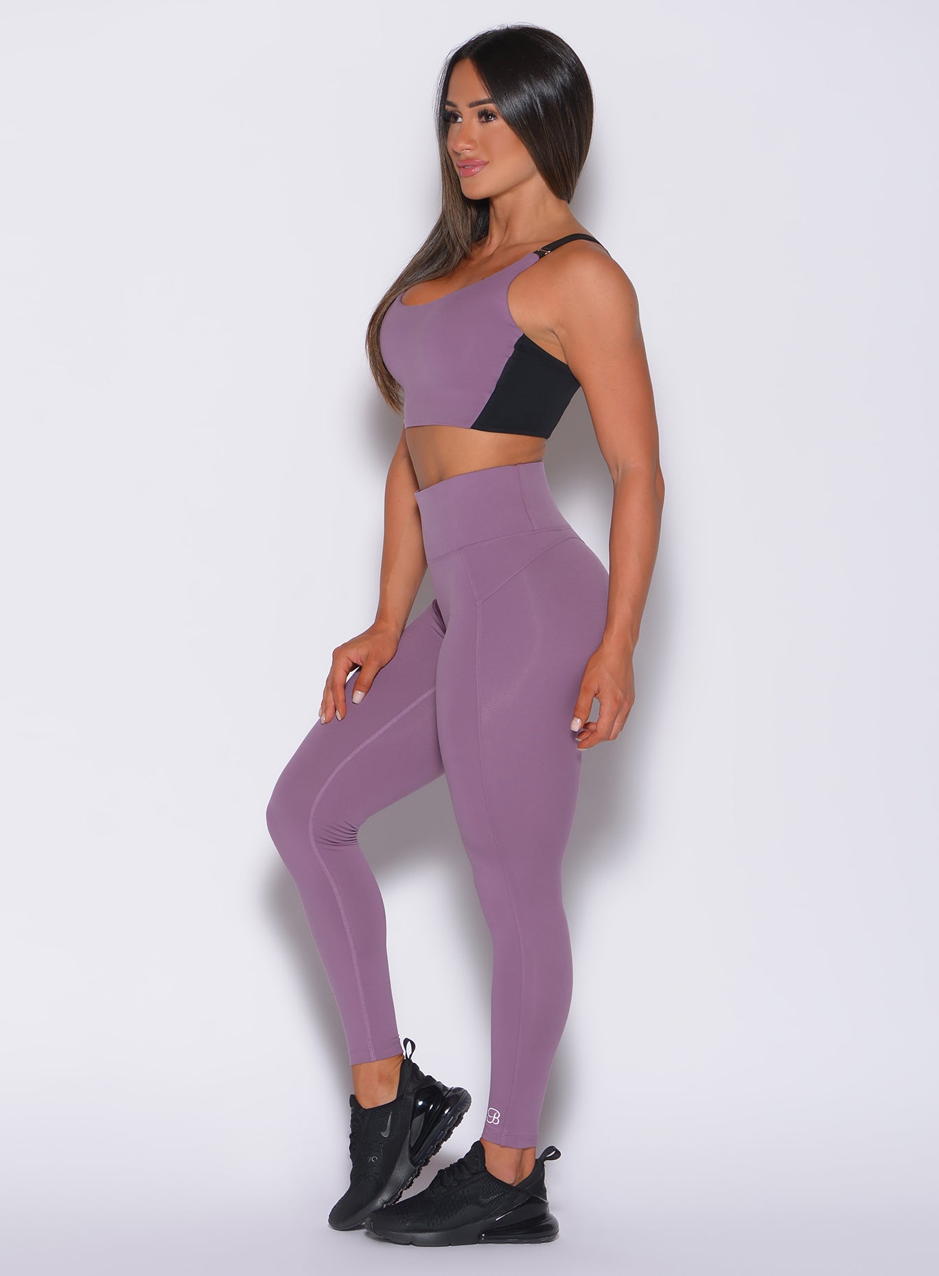 Left side profile view of a model in our snatched waist leggings in violet frost color and a matching sports bra