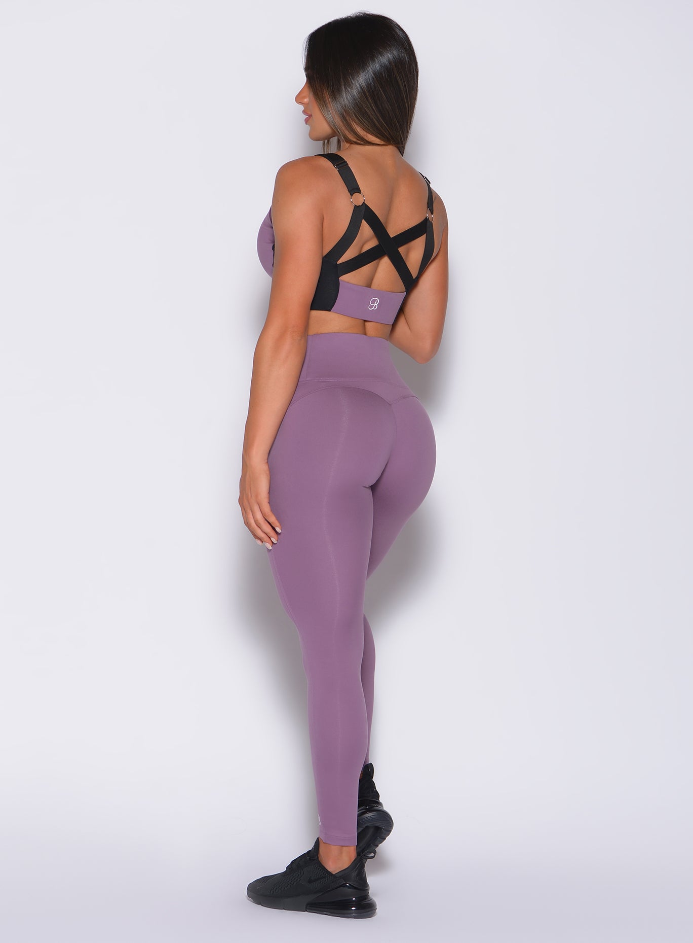 Left side profile view of a model in our snatched waist leggings in violet frost color and a matching bra