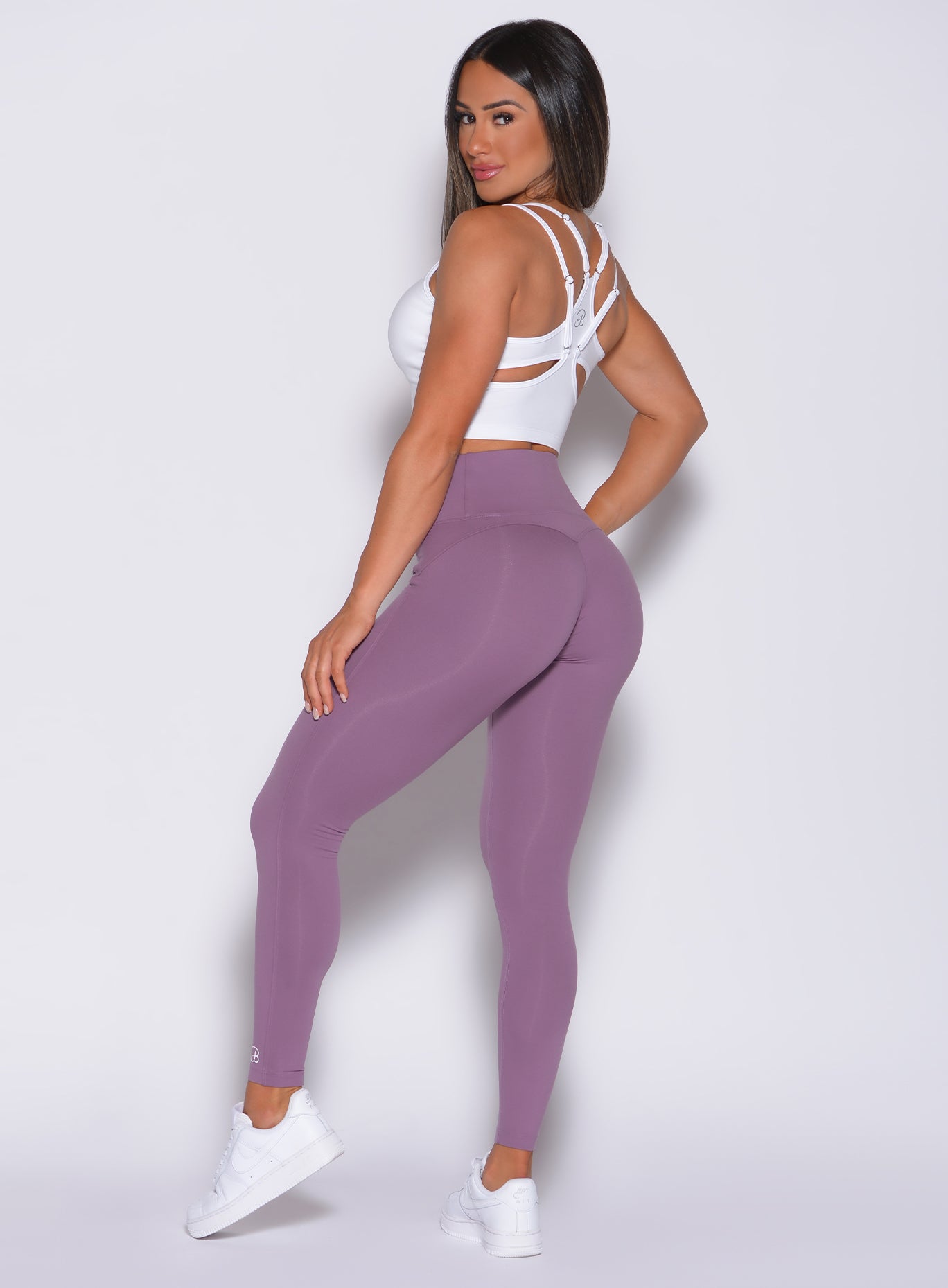 Left side profile view of a model in our snatched waist leggings in violet frost color and a white sports bra 