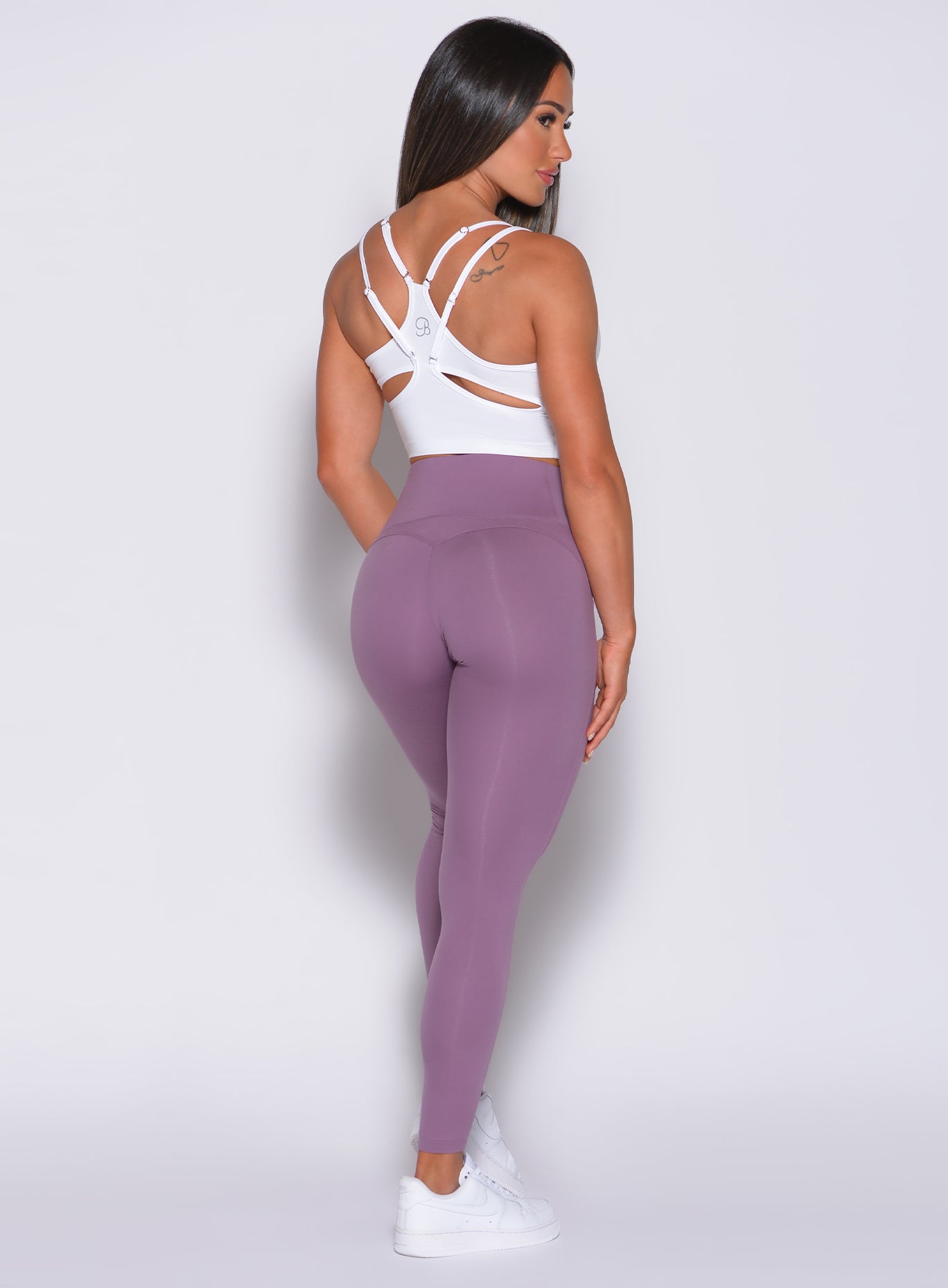 Back profile view of a model in our snatched waist leggings in violet frost color and a white sports bra
