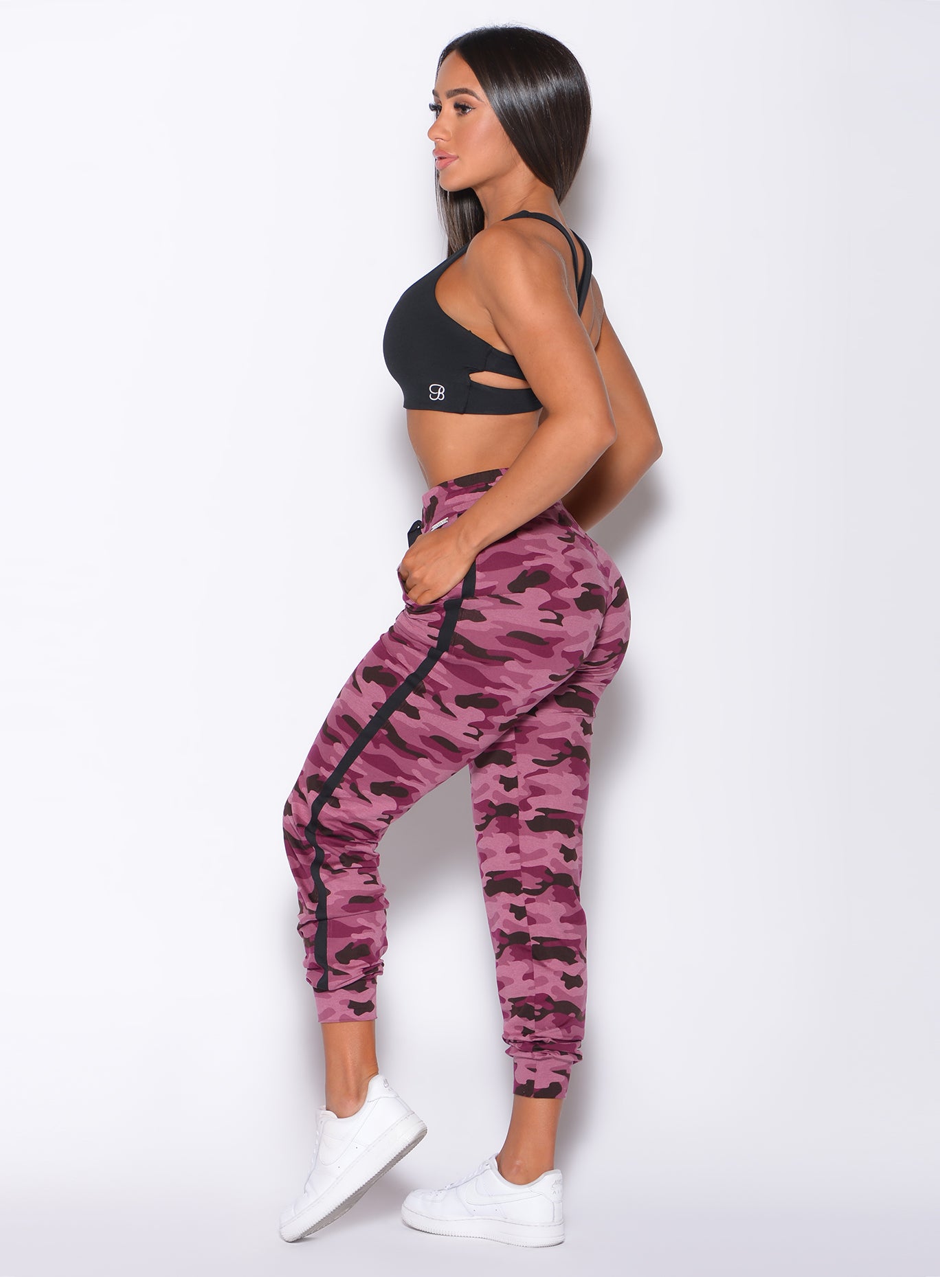 Left side  profile view of a model facing forward wearing our dream joggers in Purple Power Camo color and a black bra