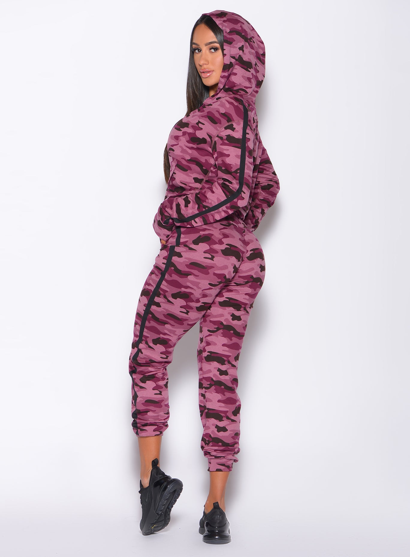 Left side profile view of a model with her hands on waist wearing our dream jacket in Purple Power Camo color and a matching joggers