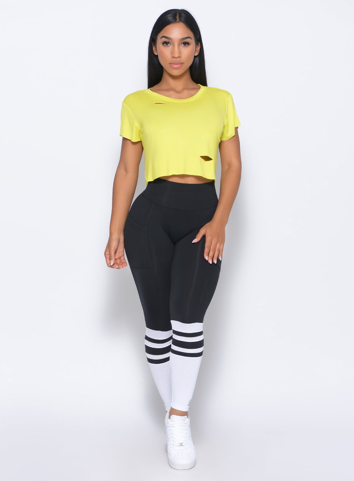 Model facing forward wearing our shredded tee in neon yellow and a black sock leggings