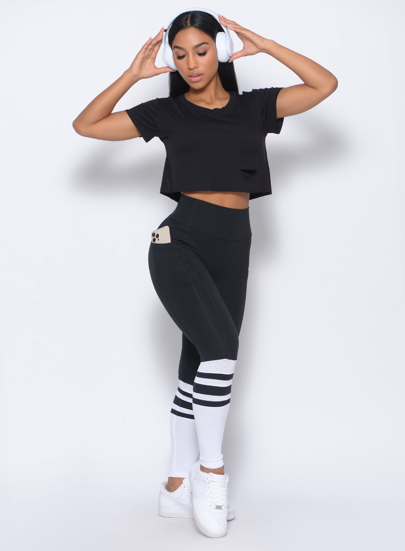 Front profile view of the model with her hands on a pair of headphones wearing our black perform sock leggings and a matching top