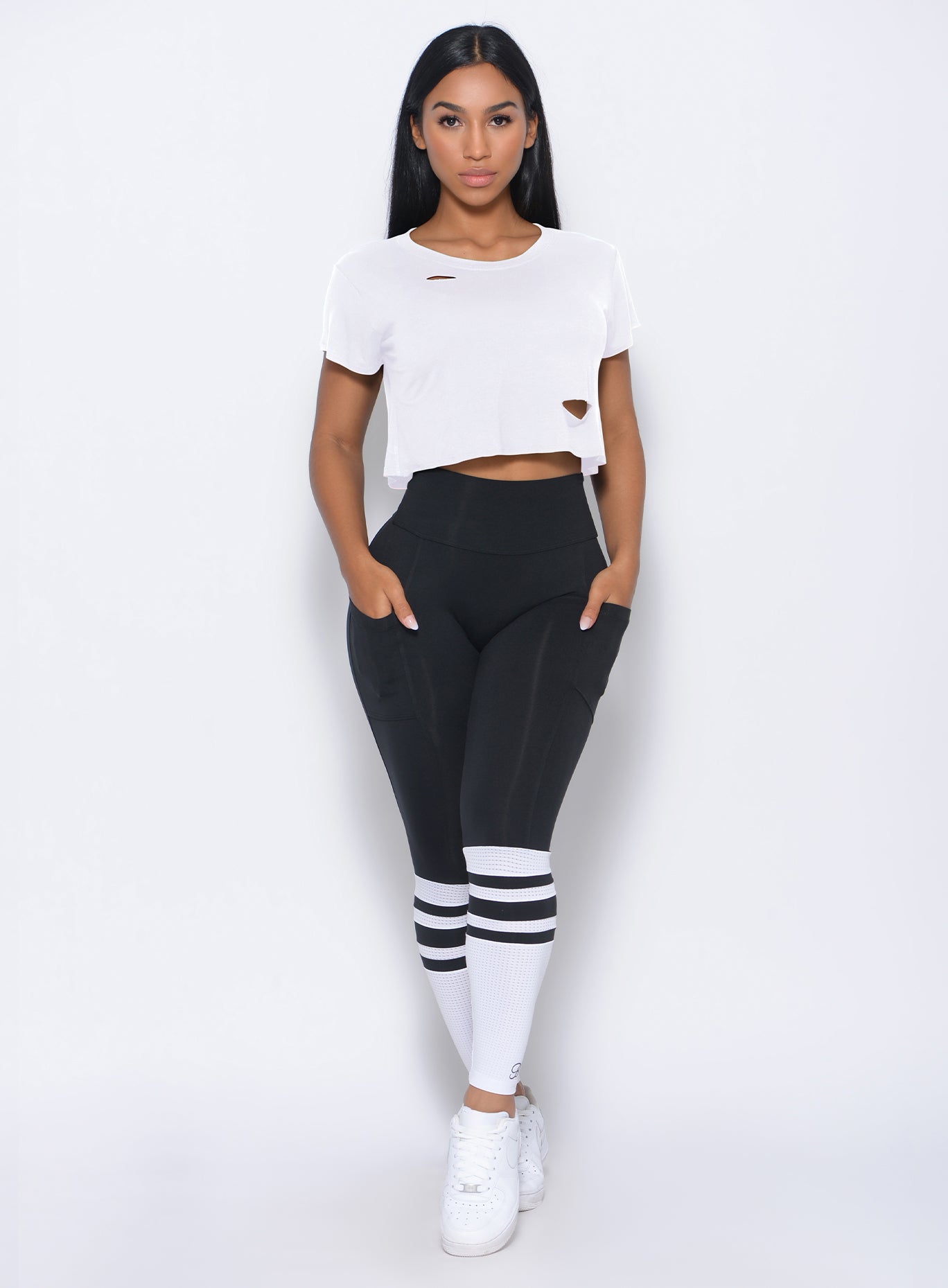 Model facing forward with her hands in pocket wearing our black perform sock leggings and a white top 