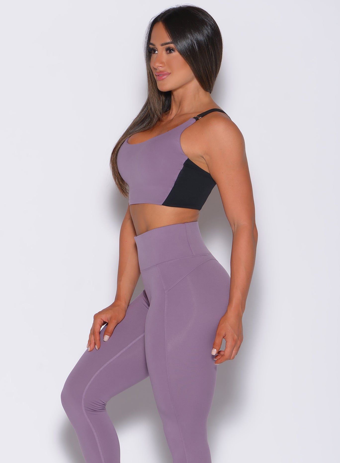 Left side profile view of a model in our banded sports bra in violet frost color and a matching leggings