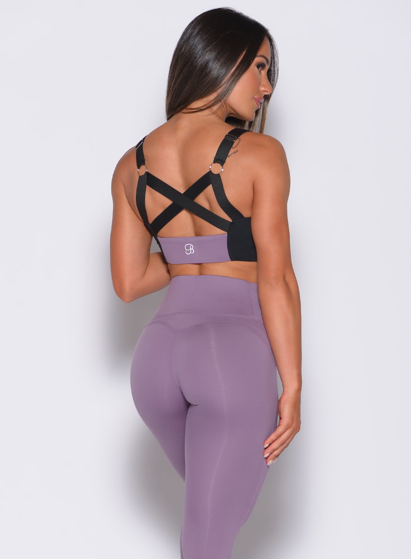 Back profile view of a model facing to her right wearing  our banded sports bra in violet frost color and a matching leggings