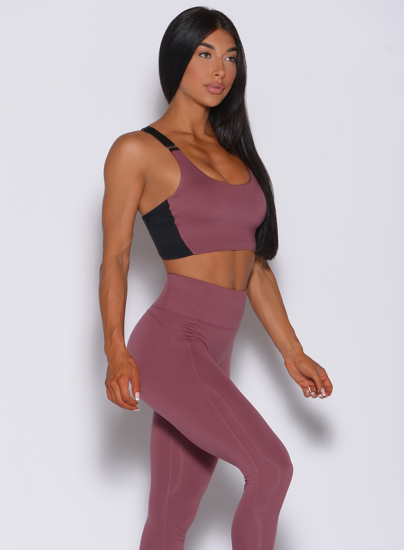 Right side profile view of a model facing forward wearing our banded sports bra in merlot color and a matching leggings