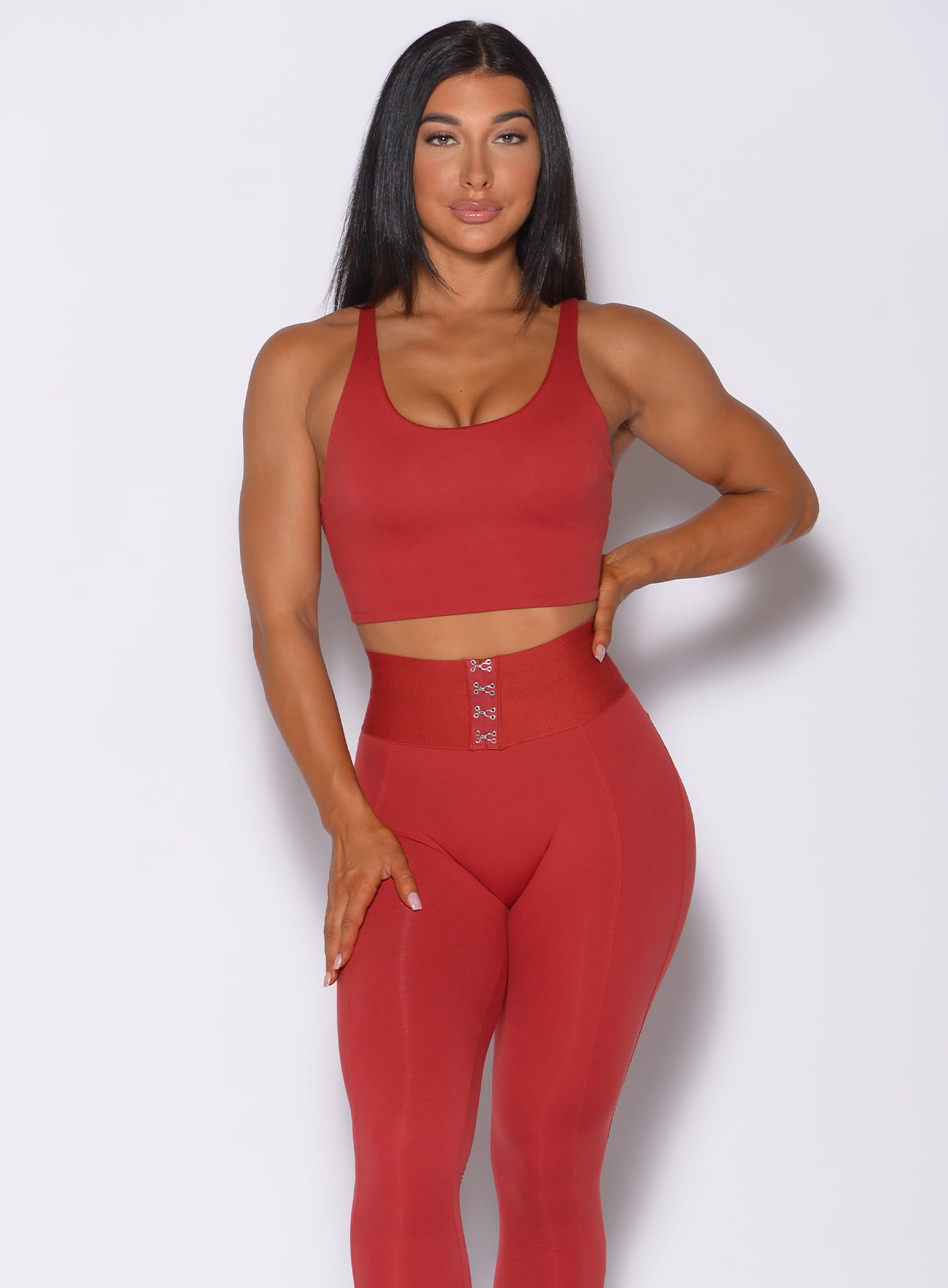 Front profile view of a model facing forward  wearing our impact sports bra in sunset red and a matching leggings