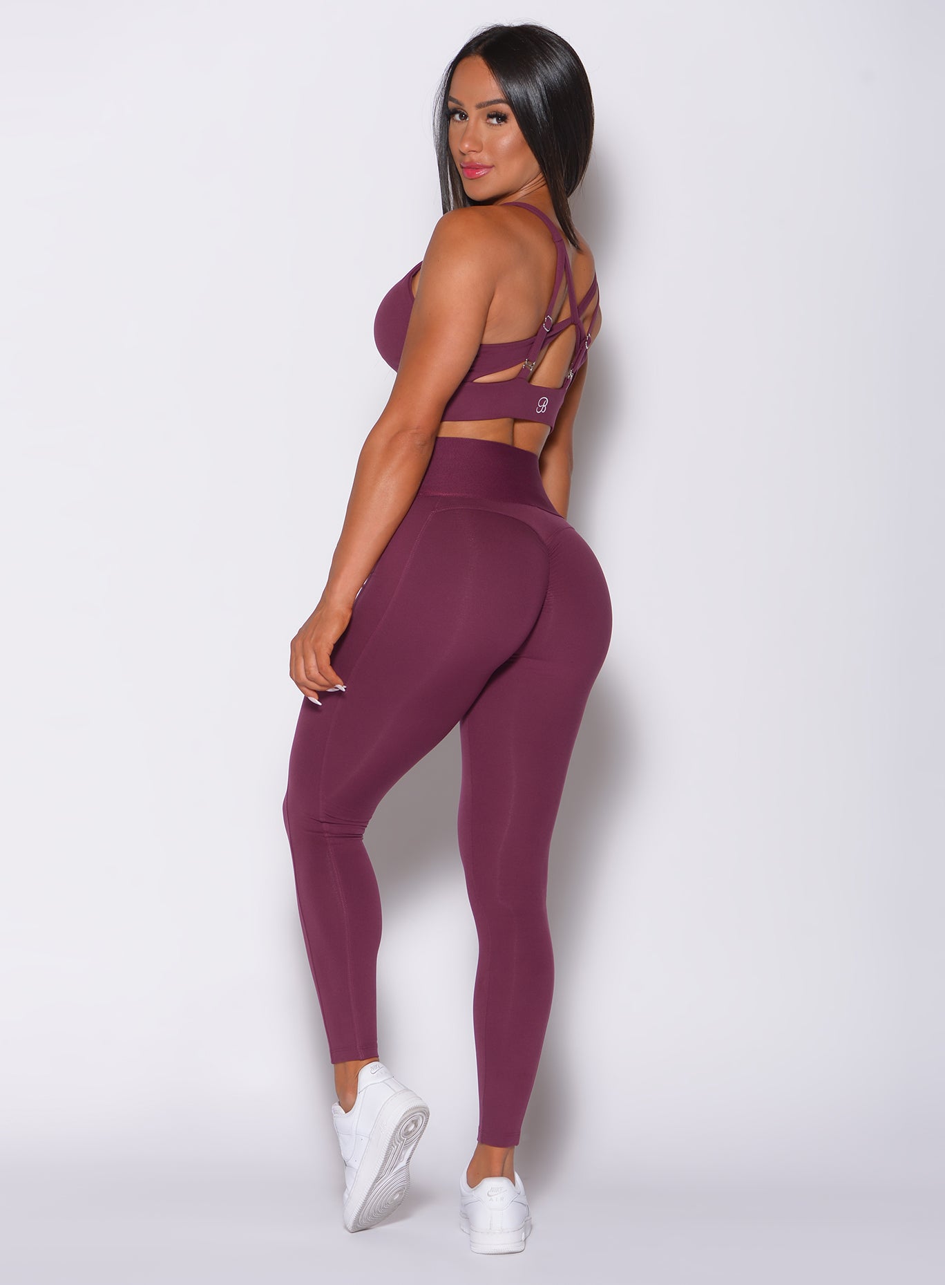 Left side profile view of a model in our waist cincher leggings in majestic purple color and a matching bra