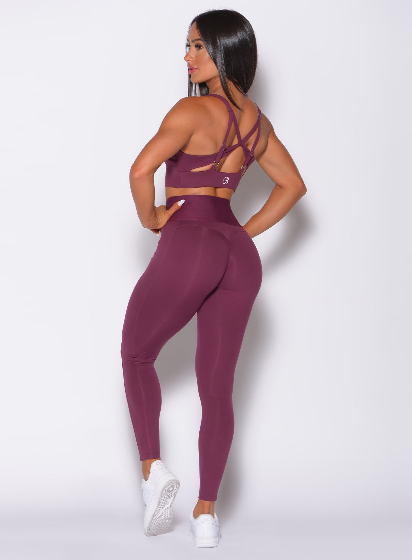 Back profile view of a model angled slightly to her left wearing  our waist cincher leggings in majestic purple color and a matching bra