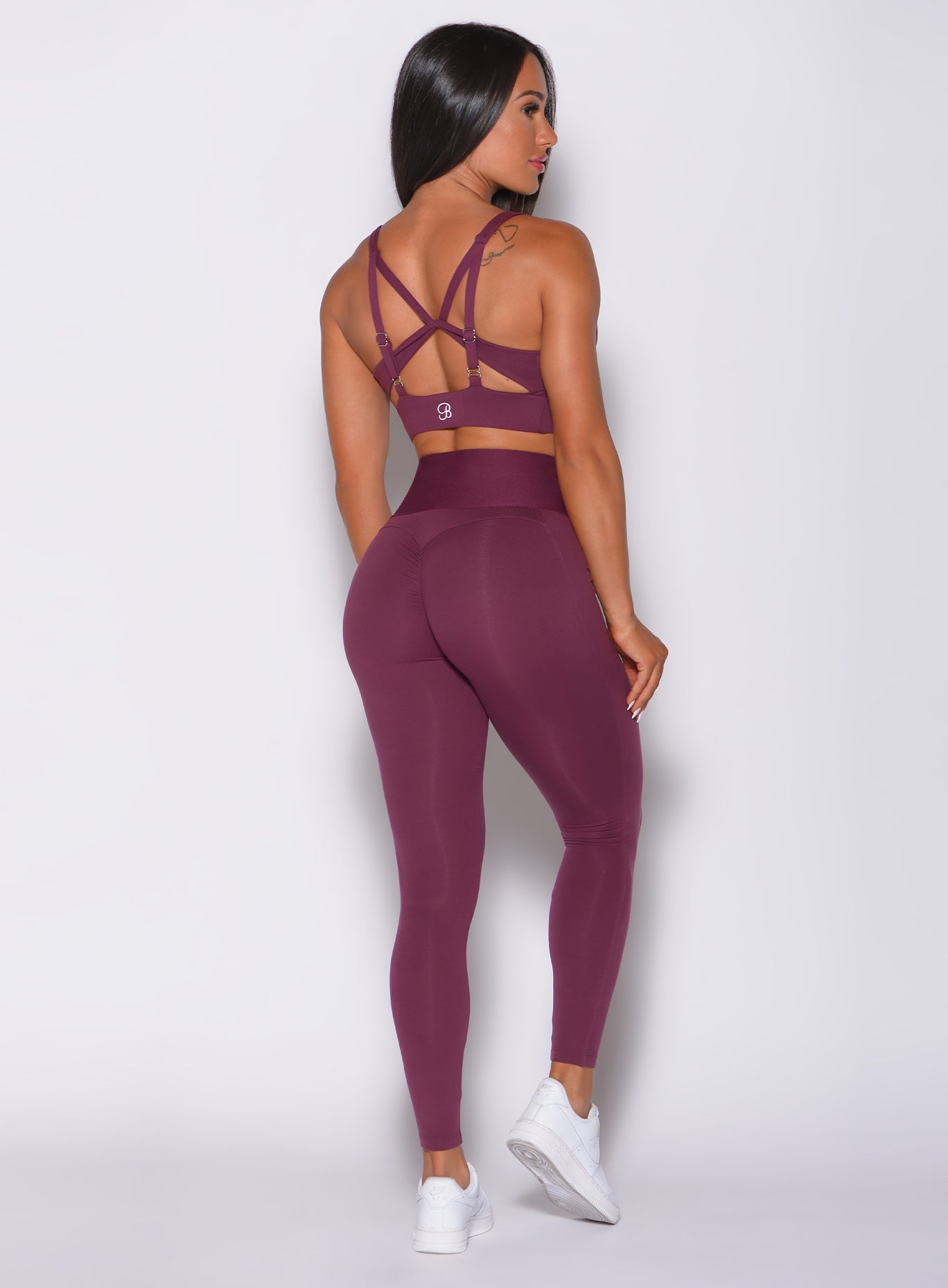 Back profile view of a model wearing our waist cincher leggings in majestic purple color and a matching sports bra