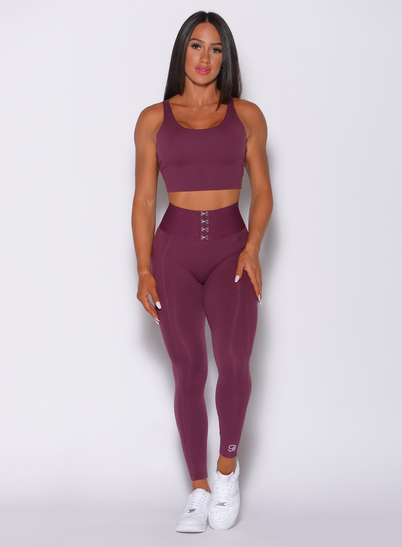 Front profile view of a model in our waist cincher leggings in majestic purple color and a matching sports bra