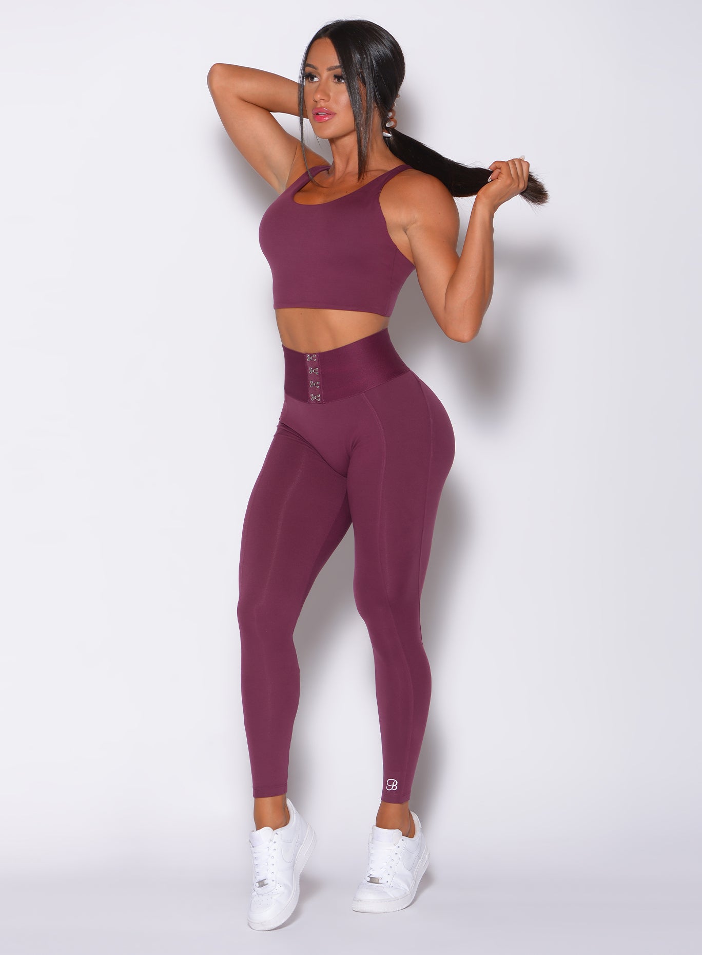 Front  profile view of a model in our waist cincher leggings in majestic purple color and a matching bra