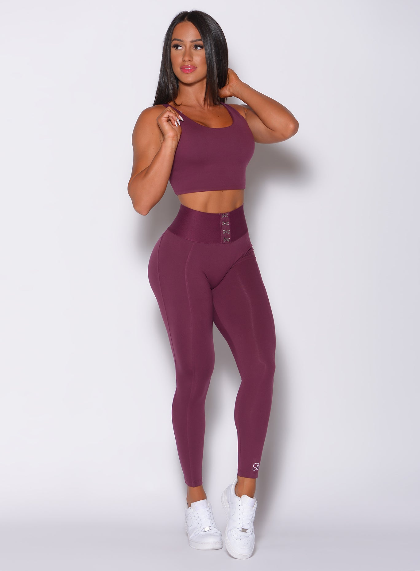 Front profile view of a model wearing our waist cincher leggings in majestic purple color and a matching bra